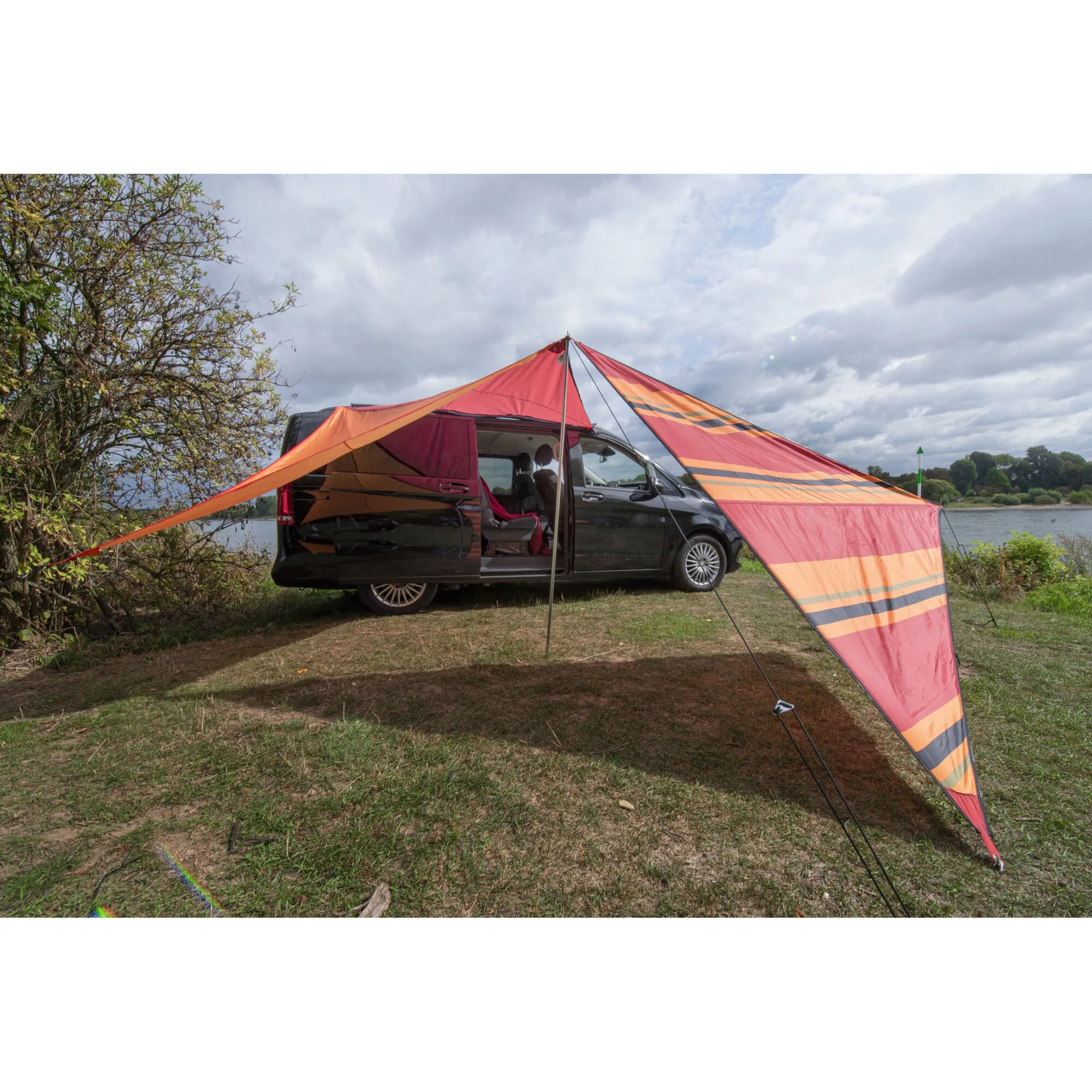 Rot-orange gestreiftes Sonnensegel Zip Canvas Oriental an einem geöffneten schwarzen Campingbus am See befestigt