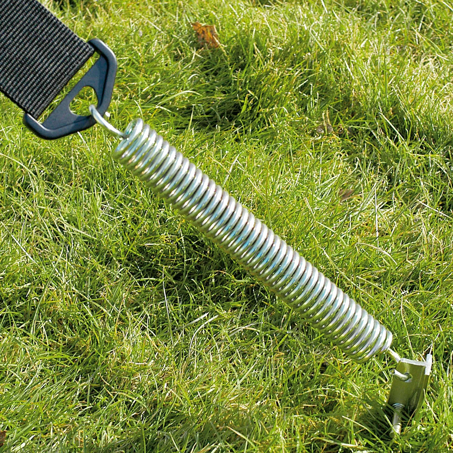 Silberne Spiral-Sturmsicherung mit Hering und schwarzer Befestigungsschlaufe auf einer Rasenfläche