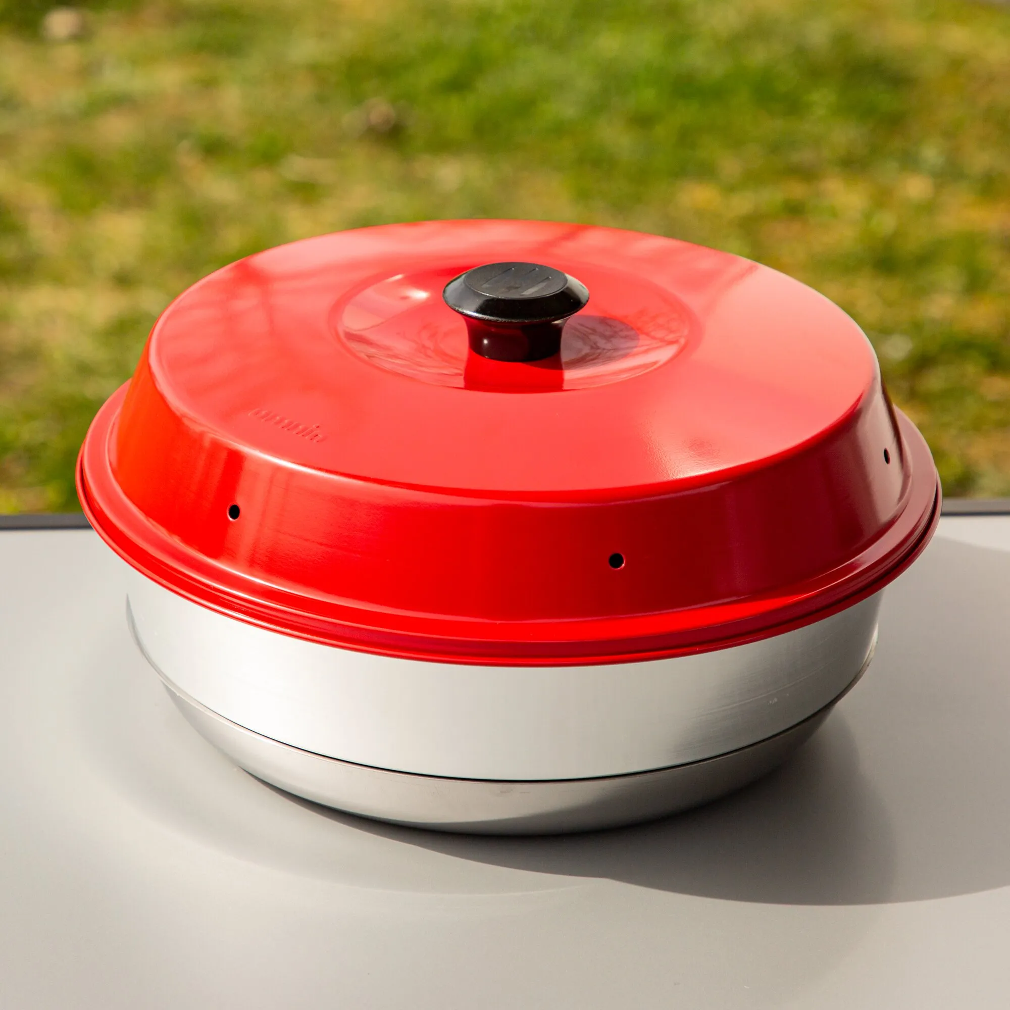 Roter runder Backofen Classic mit schwarzem Deckelgriff, Lüftungsöffnungen und silbernem Metallgehäuse auf einer Arbeitsfläche