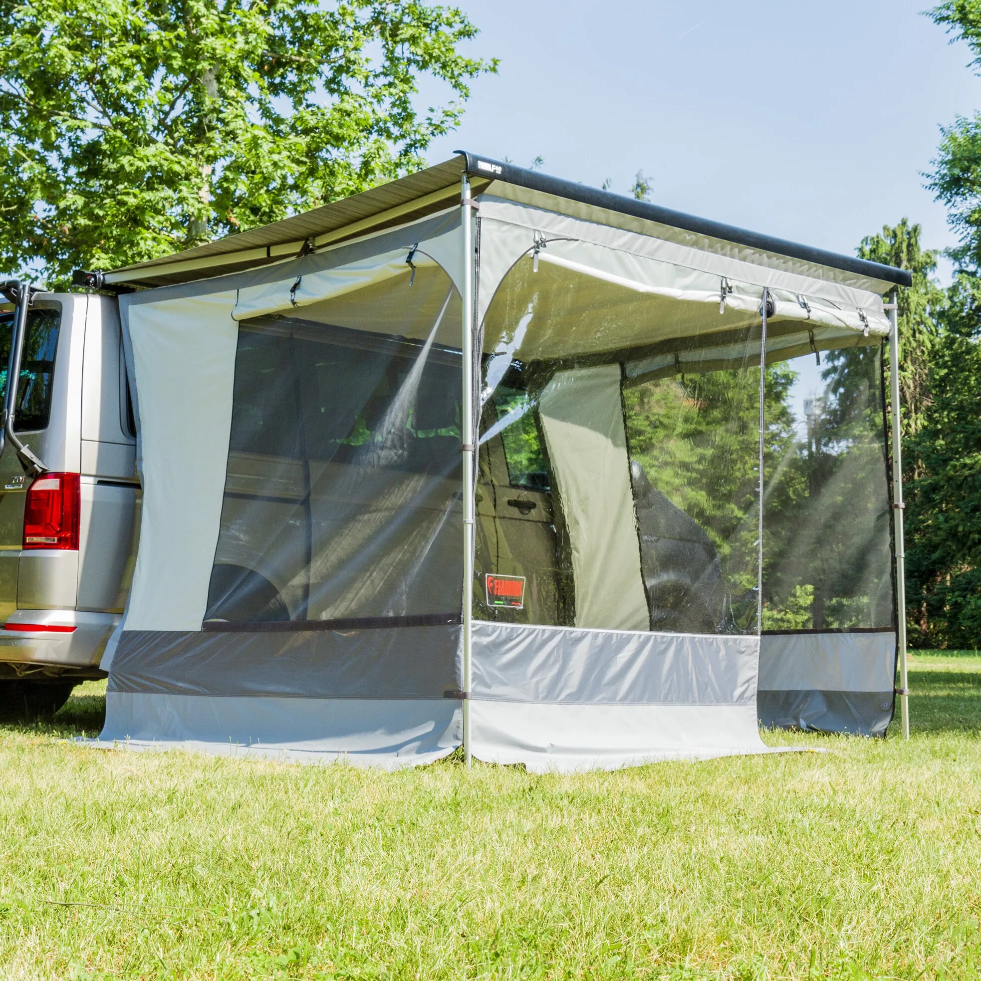 Markisenzelt Room Van Premium in Grau, an einem weißen Campingbus befestigt, mit transparenten Seitenfenstern und aufgerollten Fensterabdeckungen