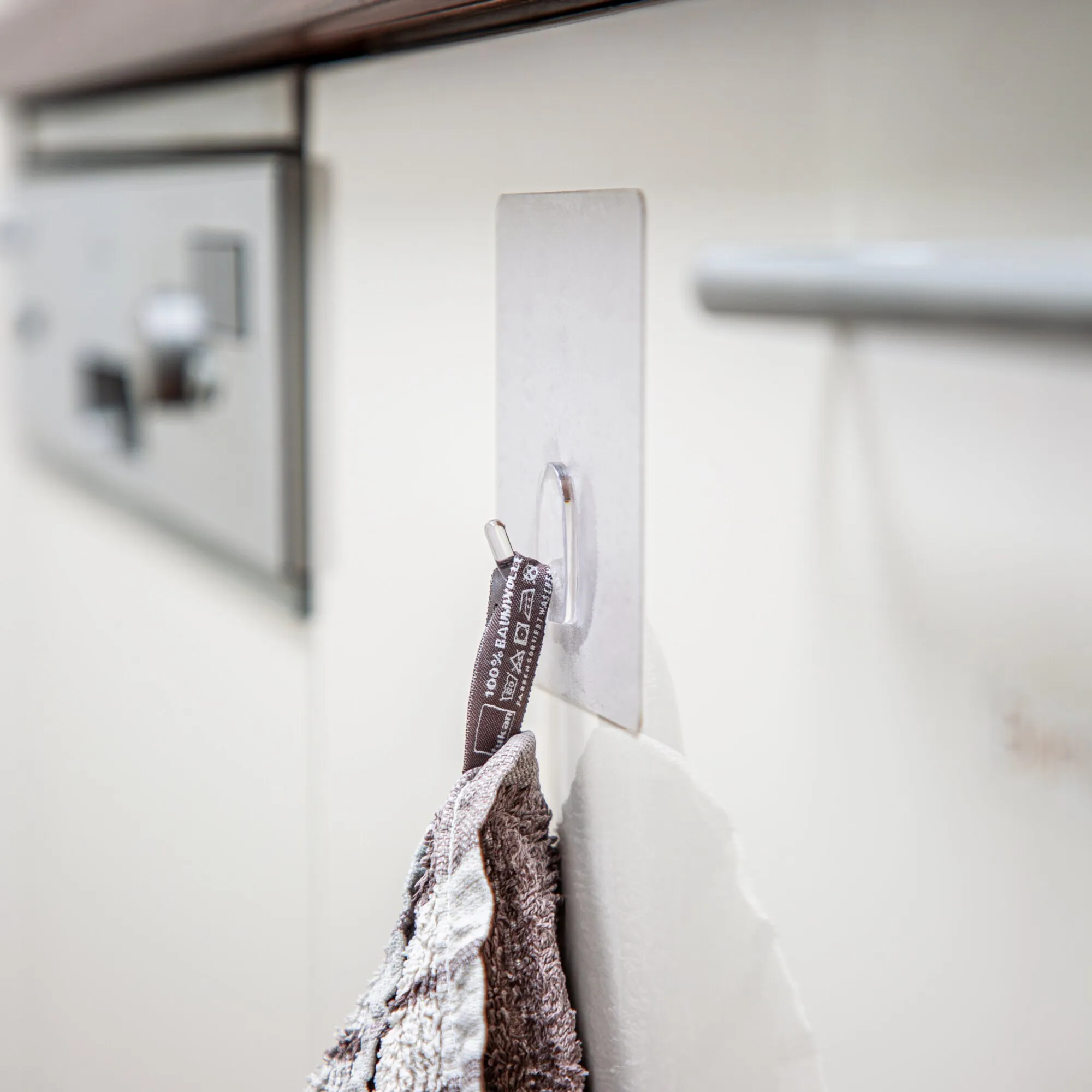 Transparenter XL-Haken an einer weißen Wand, an dem ein gemustertes Handtuch hängt; weitere Haken sind im Hintergrund sichtbar