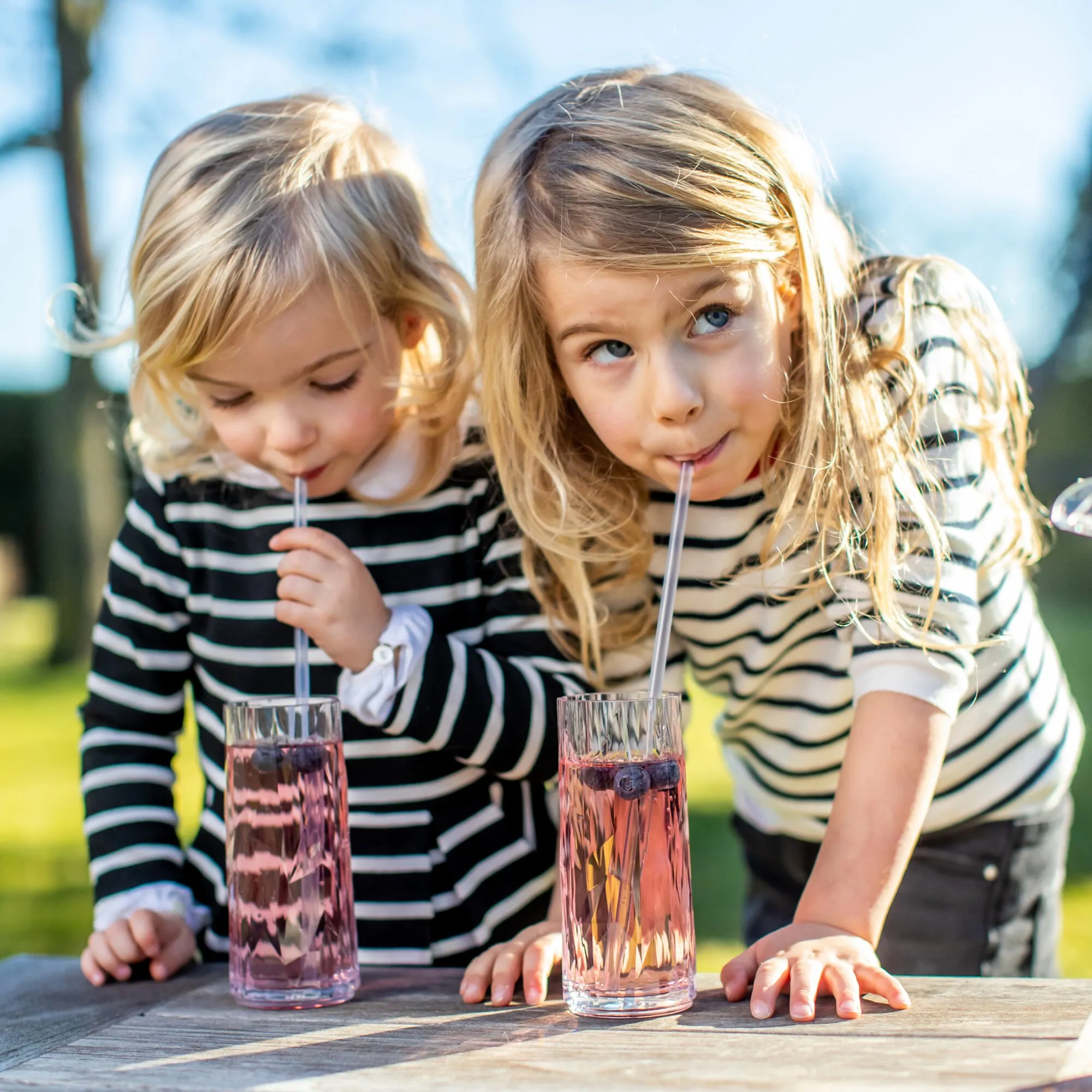 Zwei Kinder trinken im Freien durch transparente Trinkhalme aus Gläsern mit rosafarbenem Getränk, Trinkhalme CHEERS