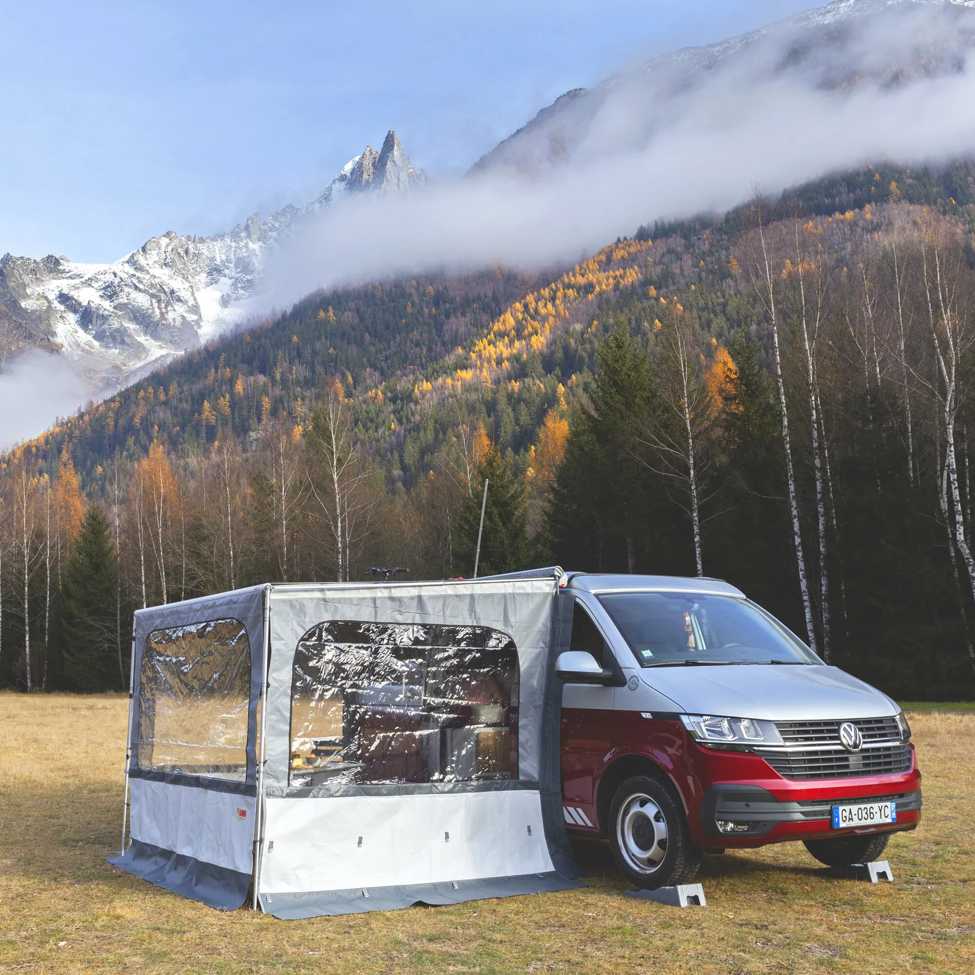 Graue Seitenwand Side W Pro F35 Van an rotem Volkswagen-Campingbus mit transparenten Fenstern vor bewaldeten, verschneiten Bergen