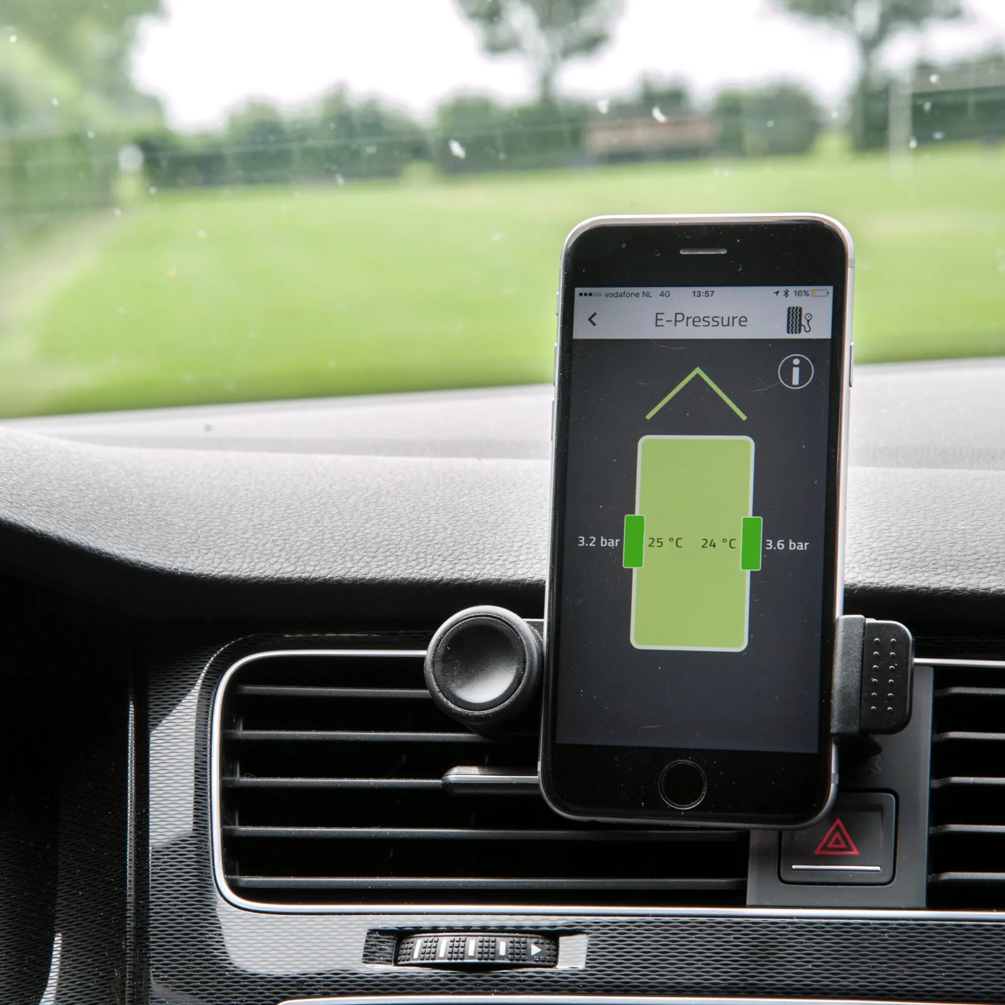 Smartphone im Auto zeigt die E-Pressure-App mit Reifendruckwerten von 3,2 und 3,6 bar sowie Temperaturen von 25 und 24 °C