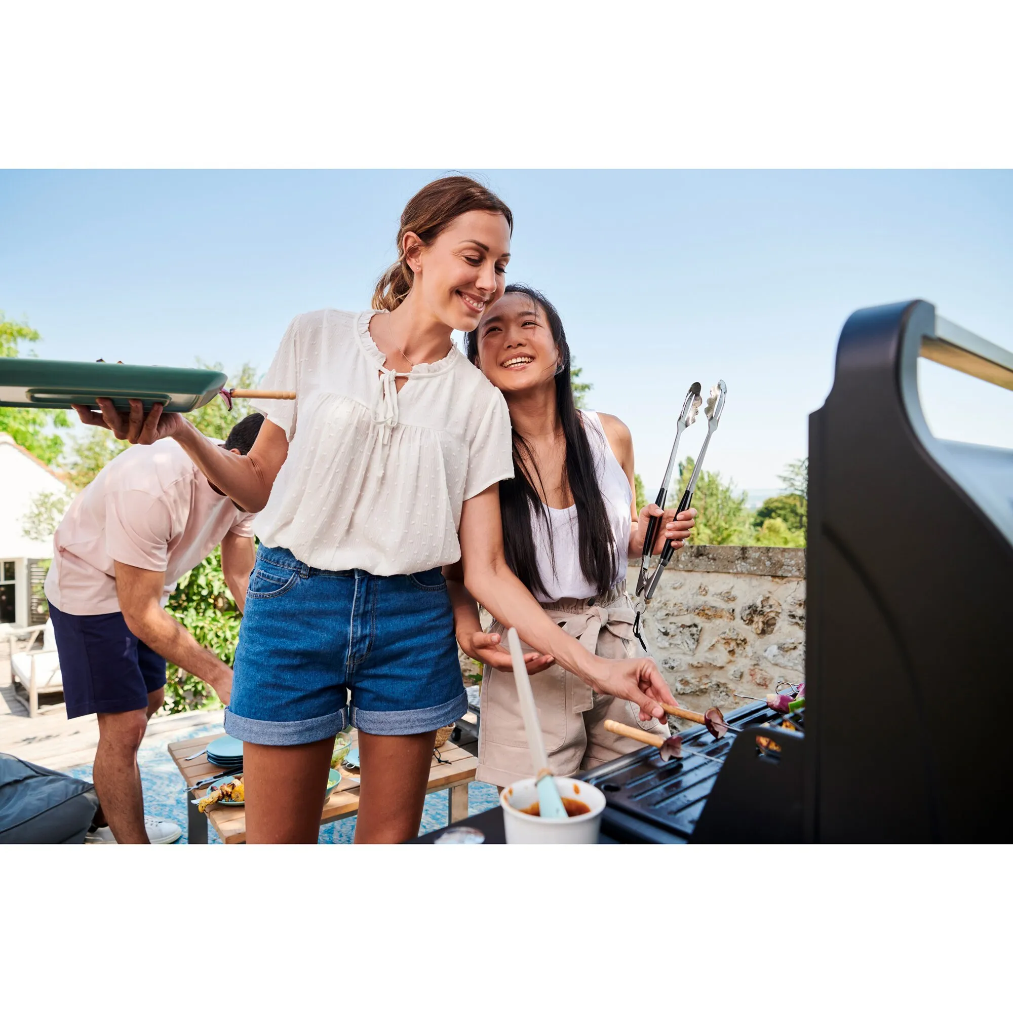Gruppe beim Grillen im Freien am schwarzen Gasgrill Compact 3 L, mit Grillzange und Teller in den Händen