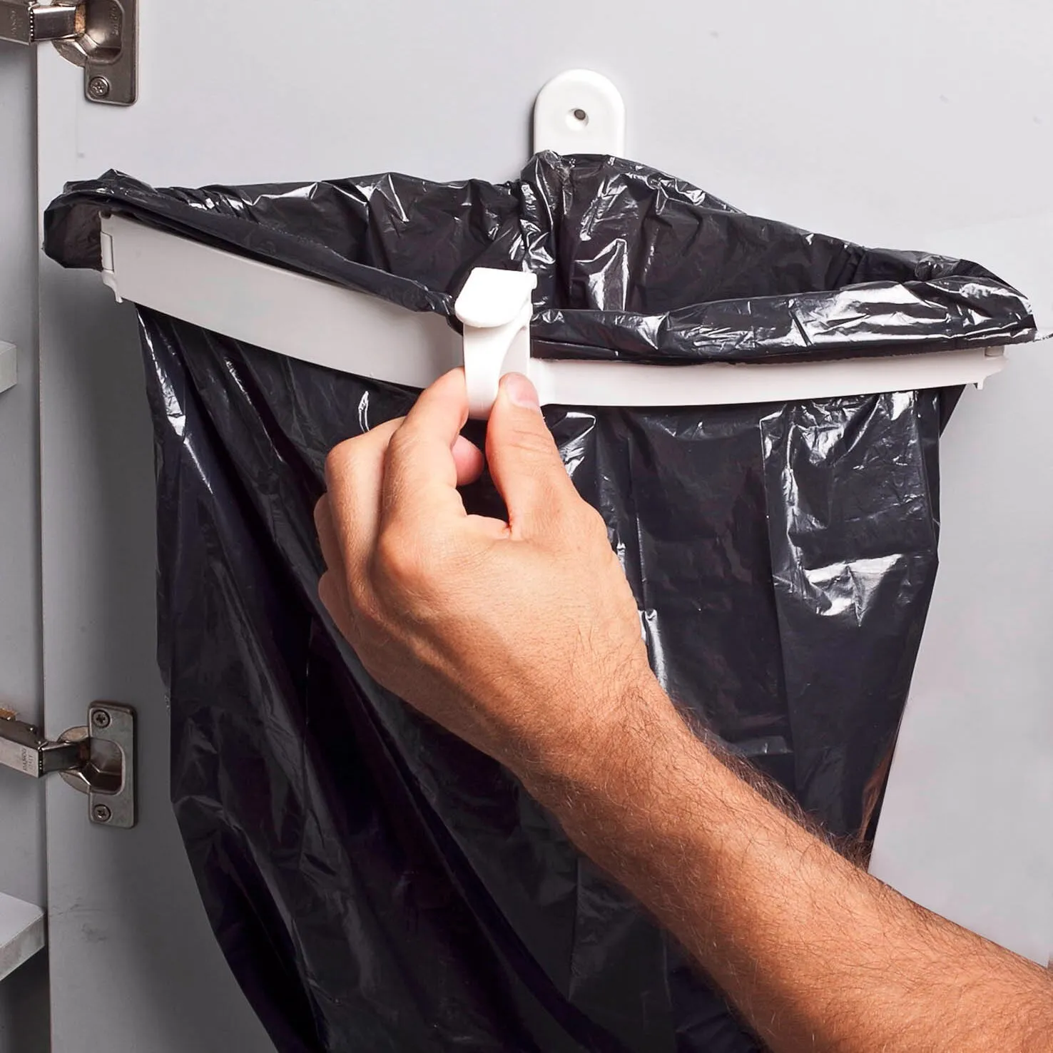 Weißer Müllbeutelhalter Snapster mit schwarzem Müllbeutel an einer Schranktür, von einer Hand am Verschluss bedient