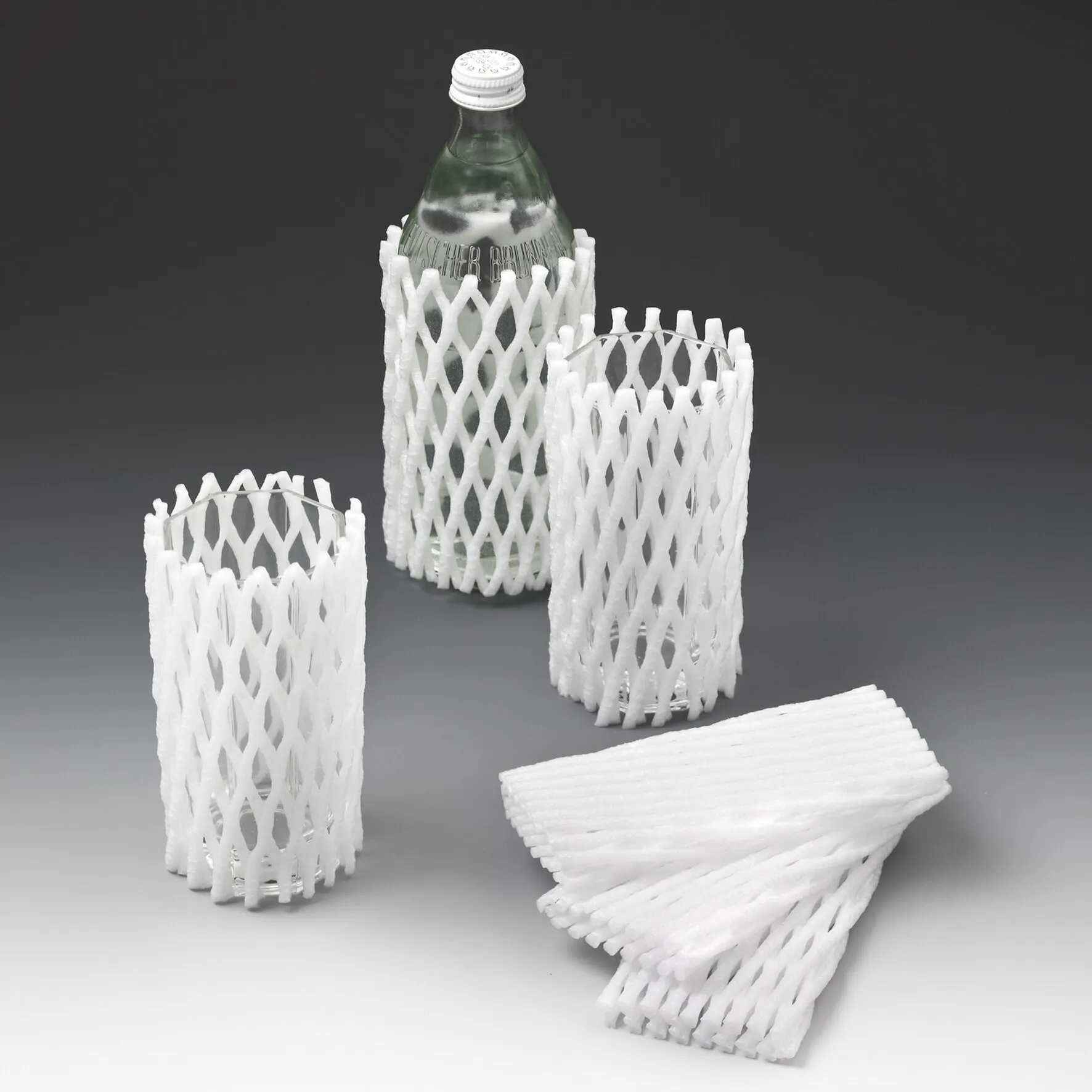Weiße Schutznetze aus Schaumstoff für Glas- und Porzellanwaren, um eine Glasflasche und drei Gläser gelegt, weitere Netze daneben