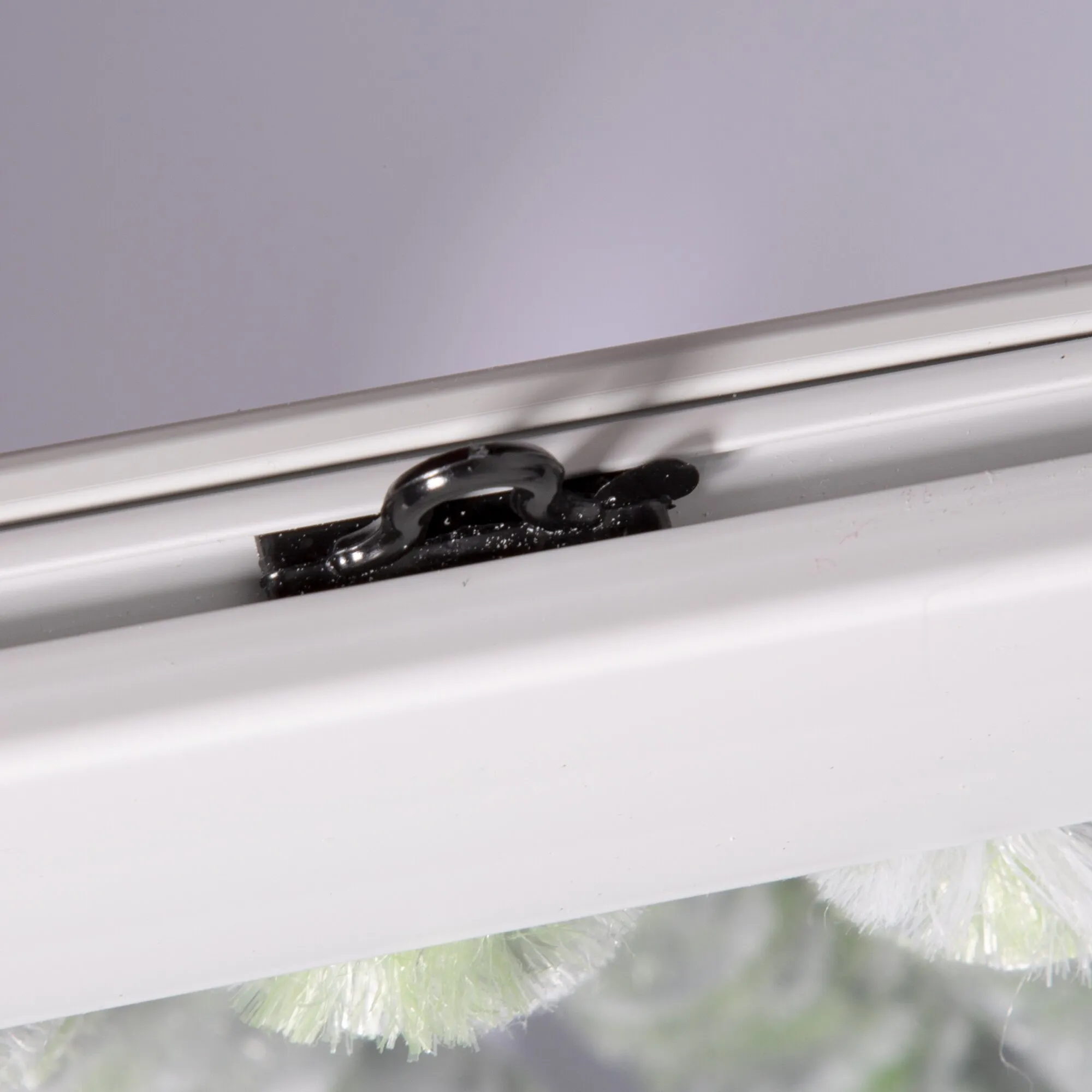 Detailaufnahme des grau-weiß-grünen Flauschvorhangs mit flauschigen Fäden an einer schwarzen Halterung am weißen Fensterrahmen