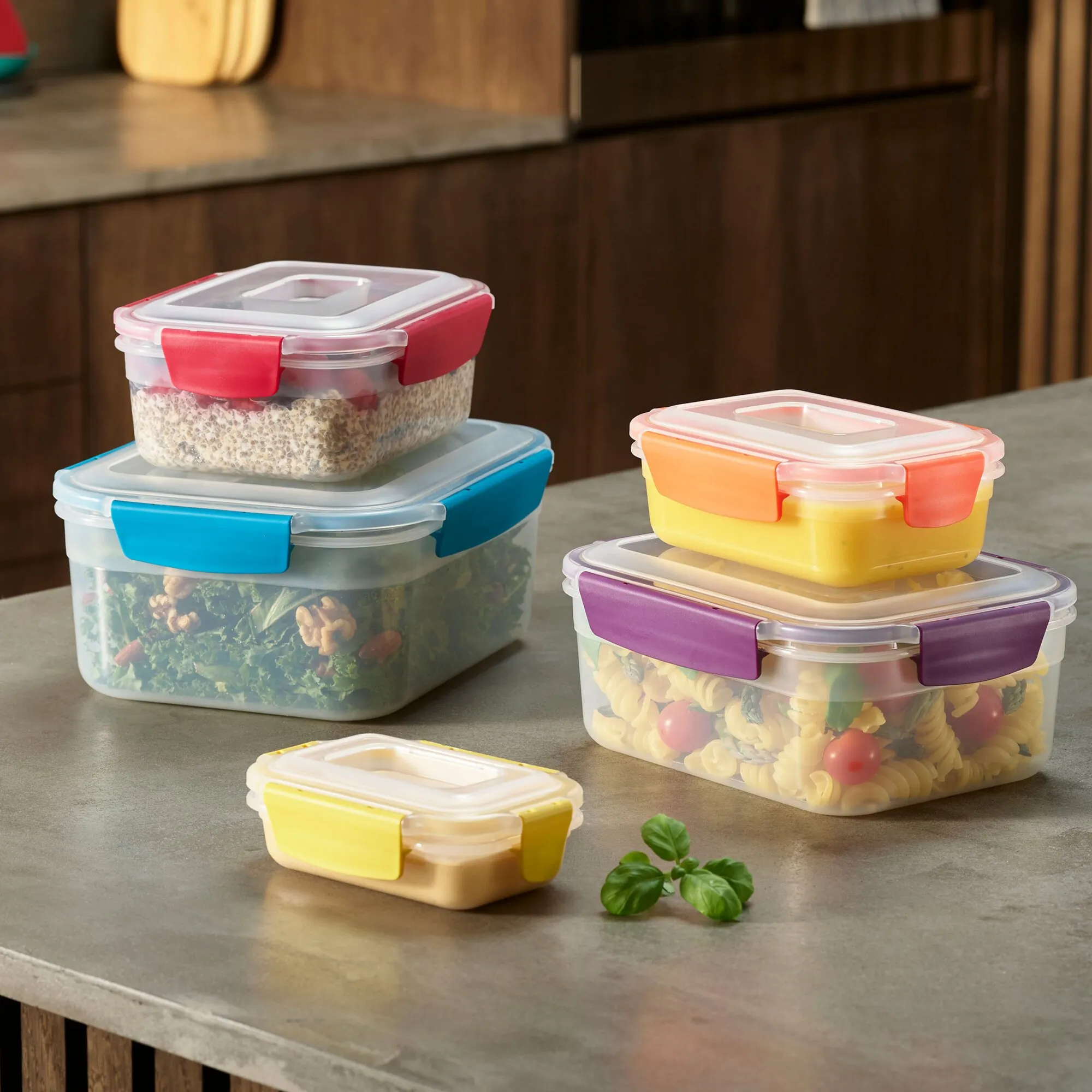 Mehrere transparente Vorratsdosen des Sets Nest™ Lock mit farbigen Verschlussclips, gefüllt mit Salat, Chiasamen, gelbem Dessert und Nudelsalat