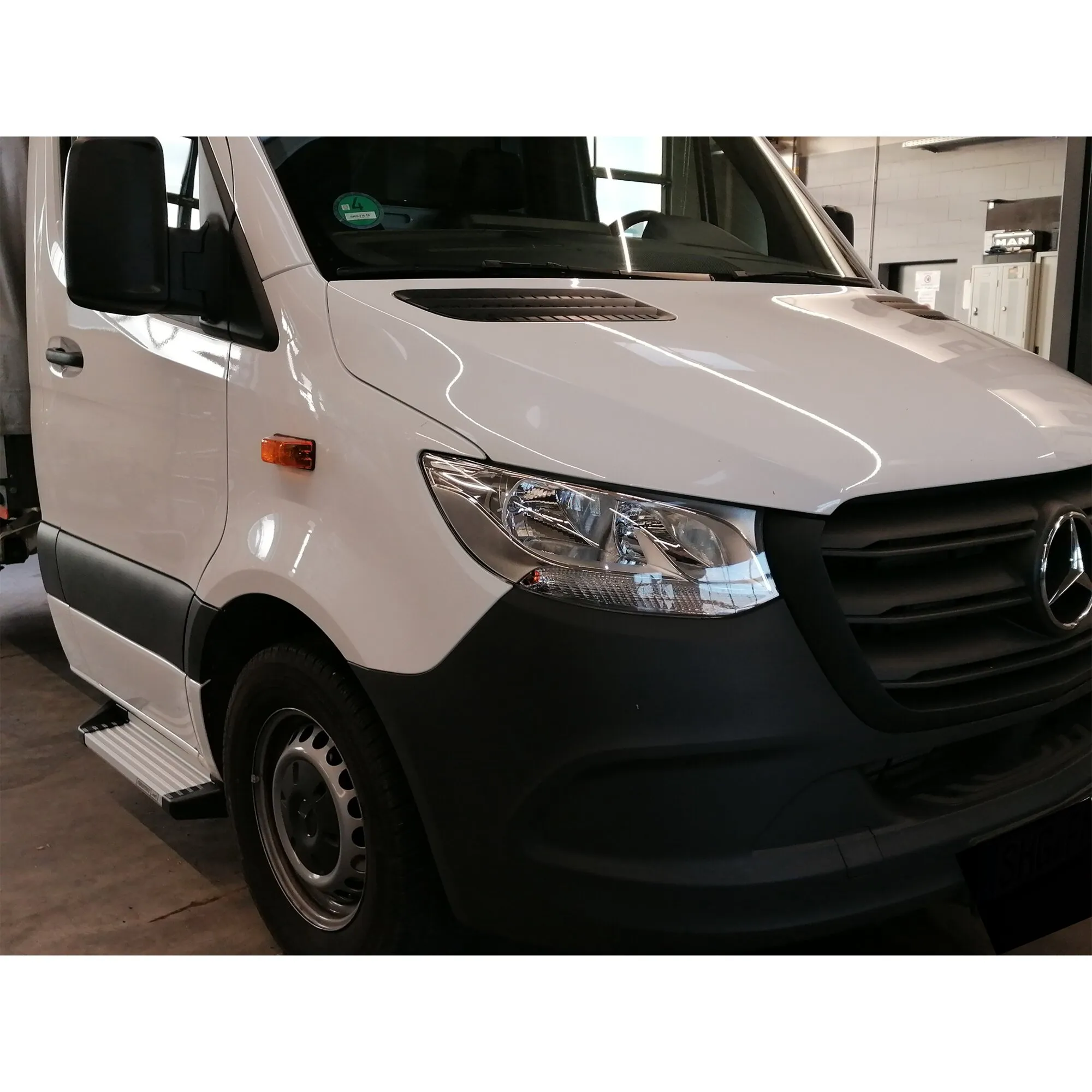 Weiße Mercedes-Sprinter-Kabine mit silberner Freistufe unter der Fahrertür, schräg von vorn aufgenommen