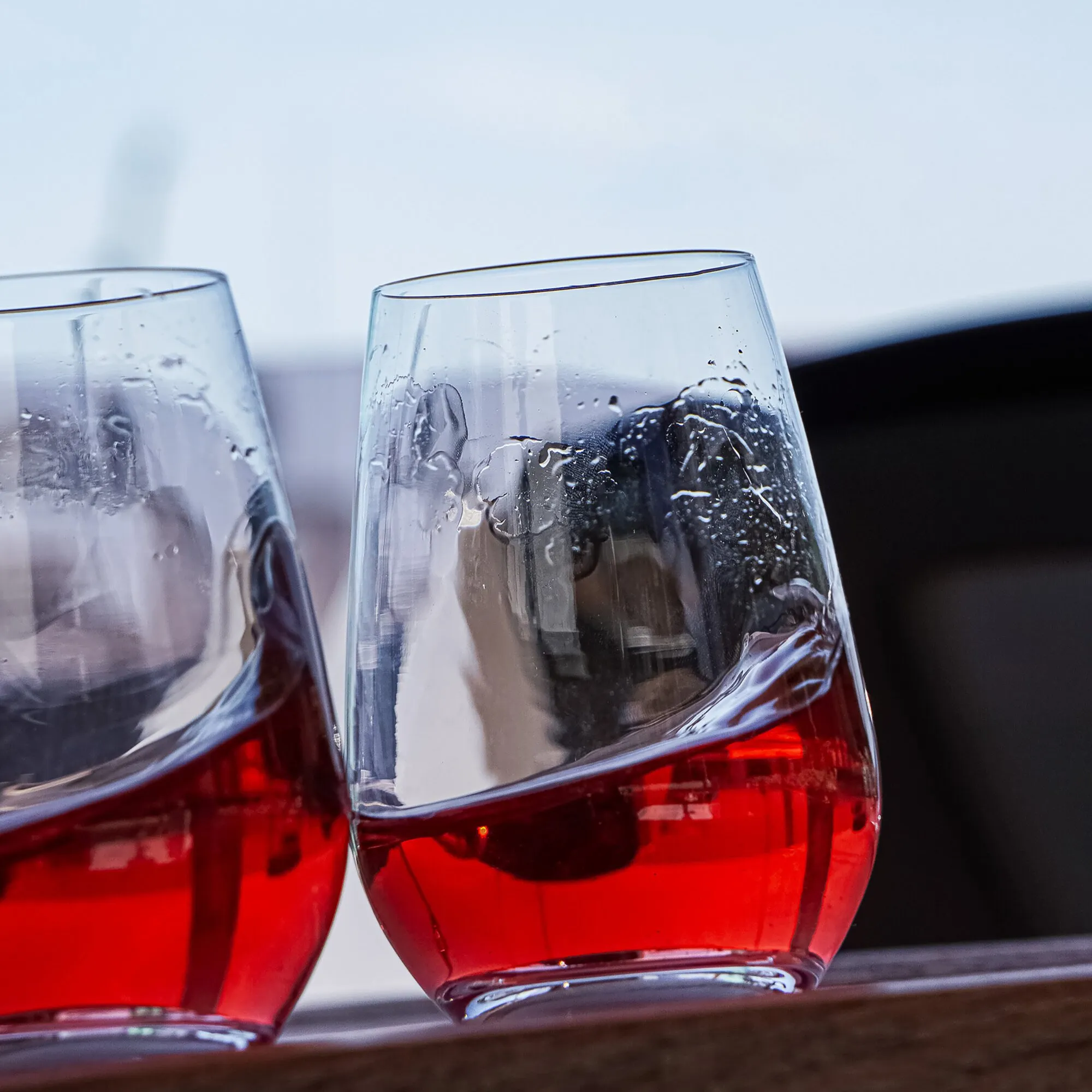 Detailaufnahme von zwei transparenten Magnet-Kristallgläsern für Longdrinks mit rotem Getränk, Eiswürfeln und Kondenswasser