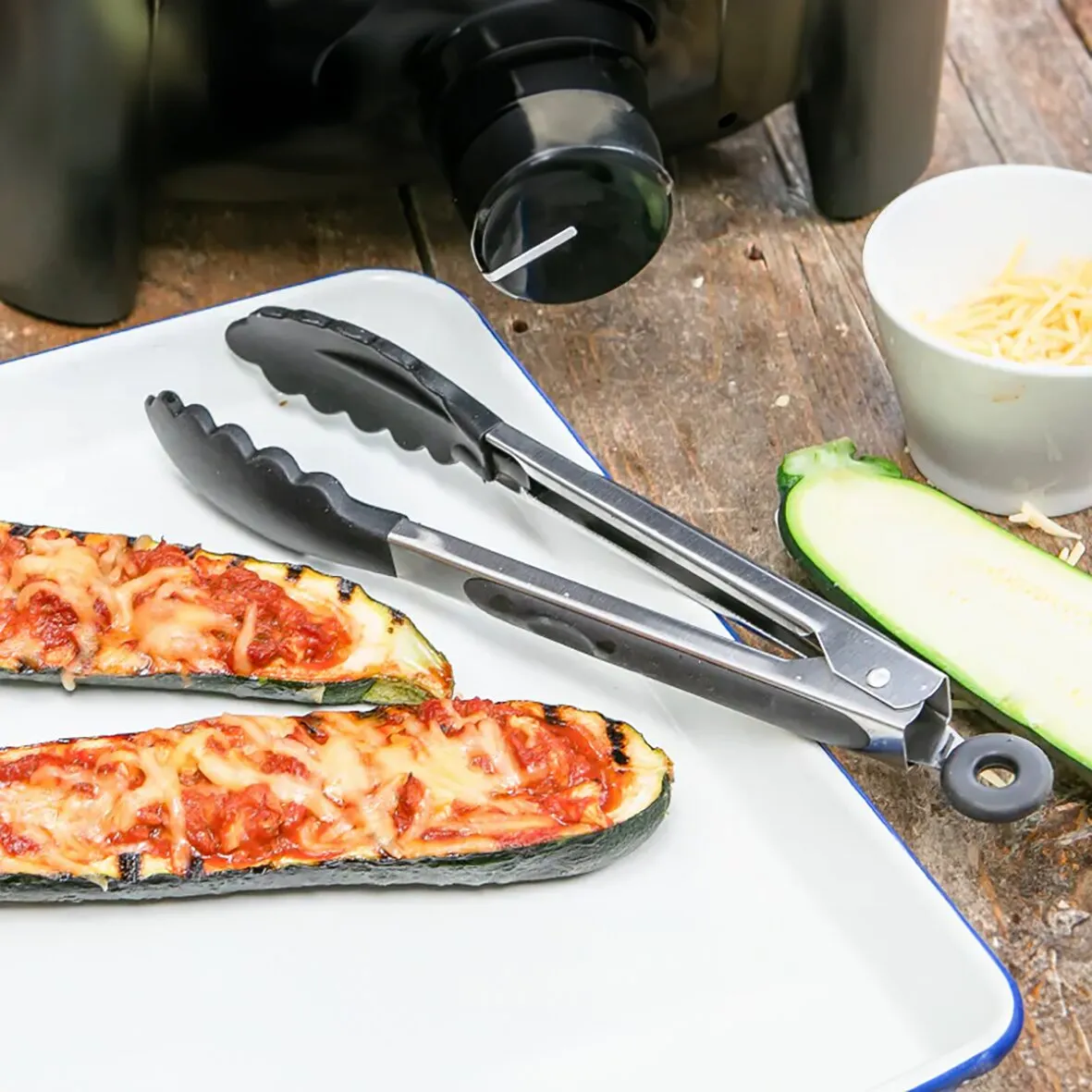 Edelstahl-Grillzange mit schwarzen Silikongreifern neben gegrillten Zucchini auf einem Teller, 280 mm lang