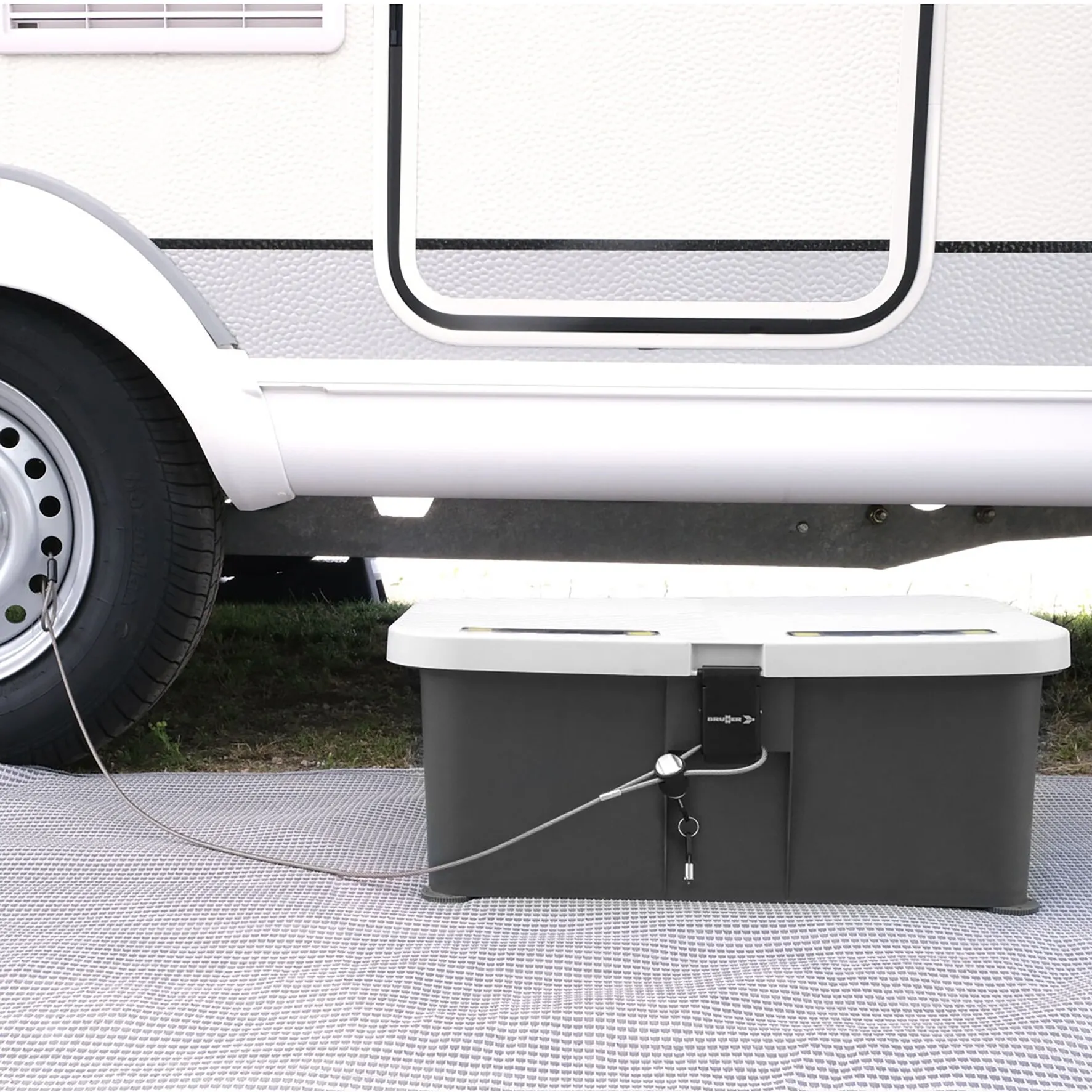 Weiße Trittstufe Boxstep NG mit schwarzem Unterkasten, Verriegelung und Stahlseil vor einem Wohnwagen in Seitenansicht