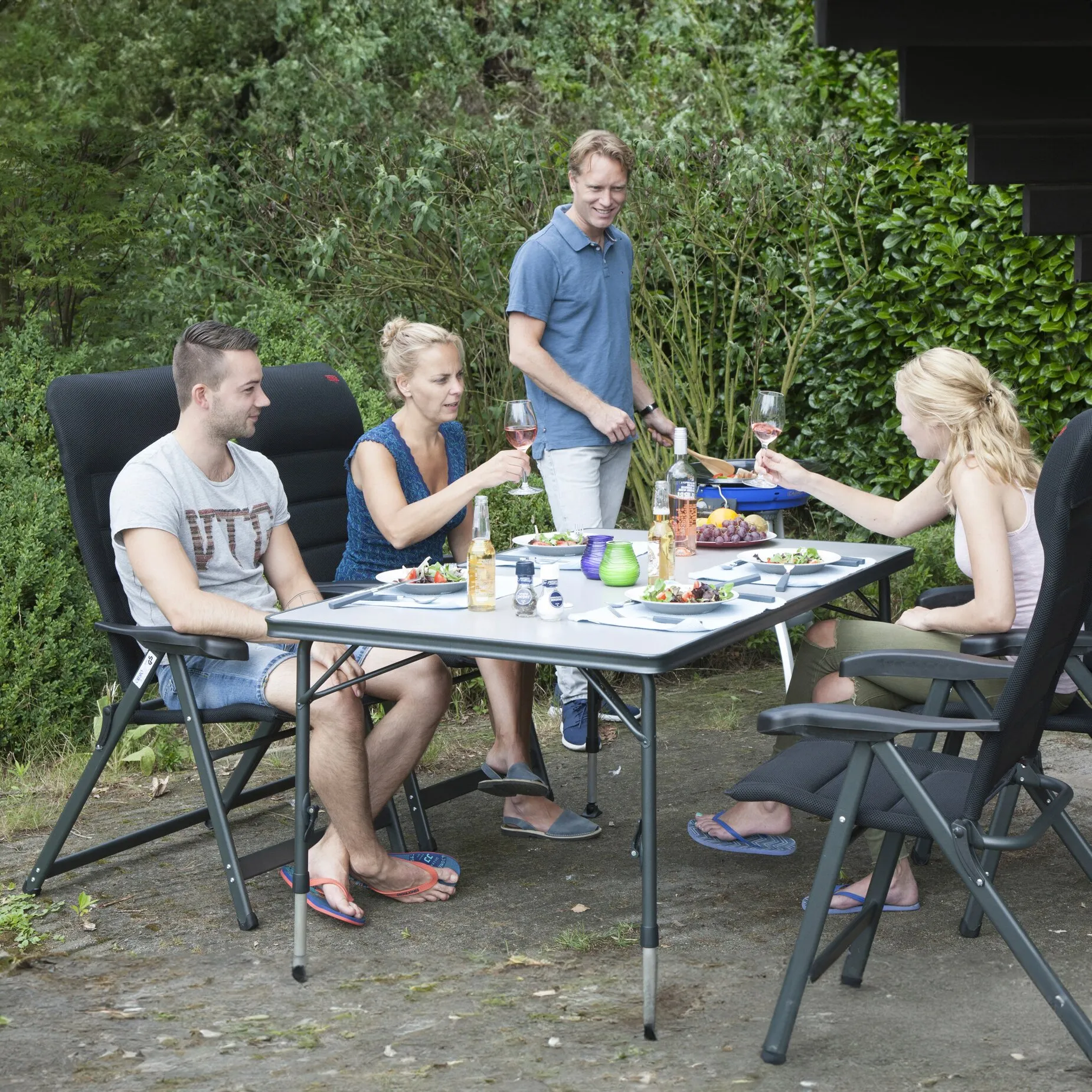 Grauer Campingtisch Crespo Sevilla 130 cm mit Klappbeinen, gedeckt mit Speisen und Getränken im Gartenbereich genutzt