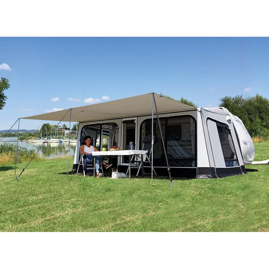 Beiges Sonnendach für den Rolli Plus, Größe 15, an einem weißen Wohnwagen am See aufgebaut, mit Tisch, Stühlen, Frau und Hund darunter