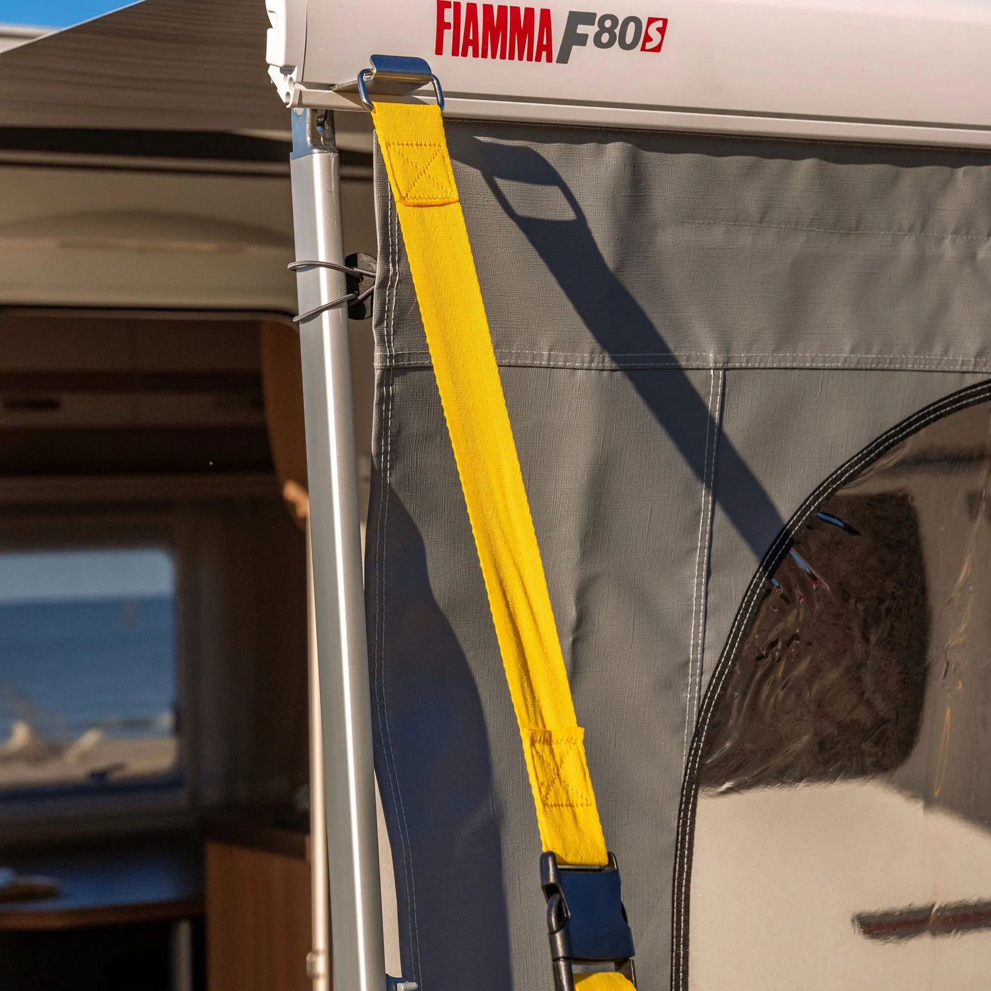 Gelbes Abspannband Tie Down S mit Schnalle an der Seitenwand eines Fiamma-F80S-Markisens befestigt