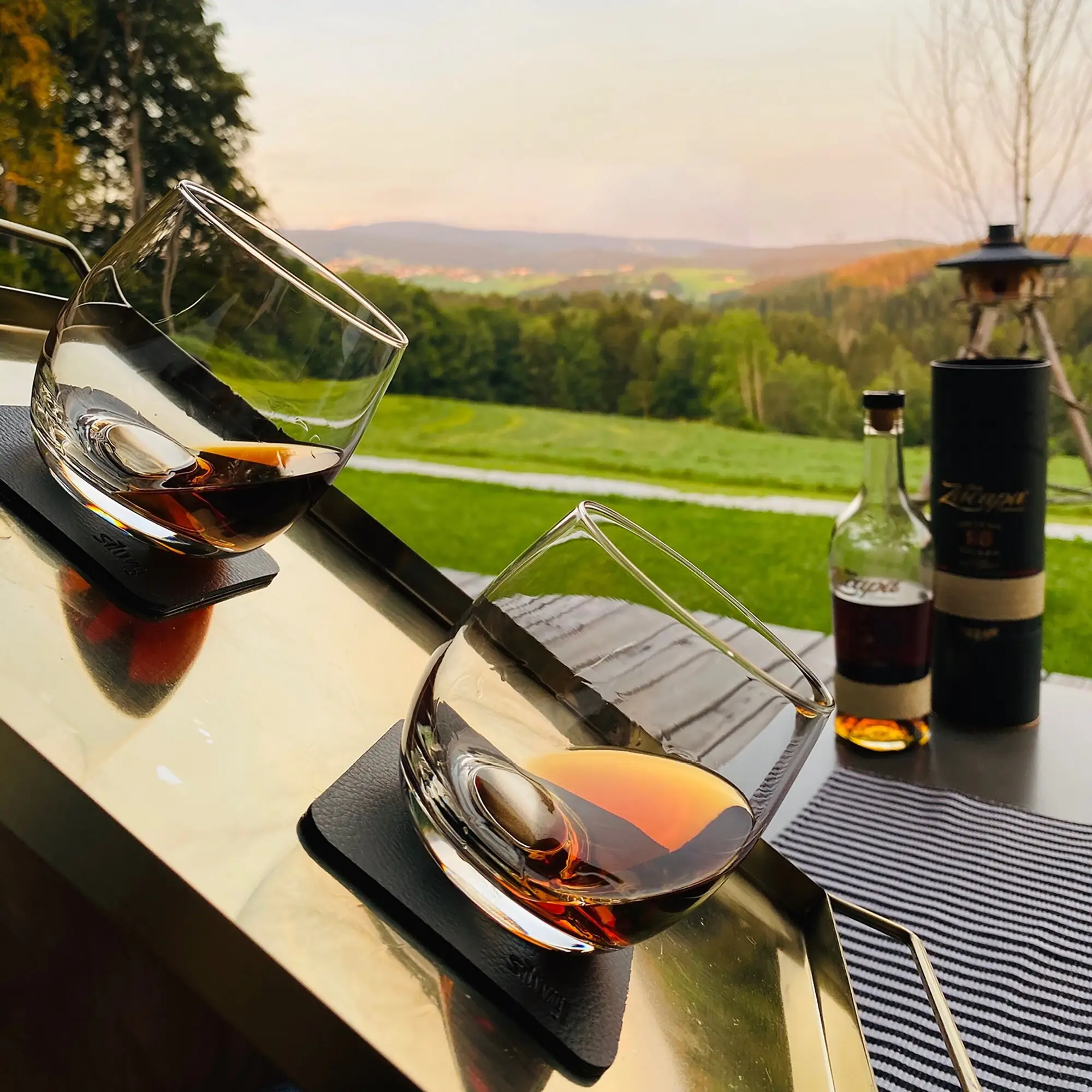 Eine Nahaufnahme eines Whiskyglases mit bernsteinfarbener Flüssigkeit auf einer glatten Oberfläche, im Hintergrund Laterne und Whisky-Flasche