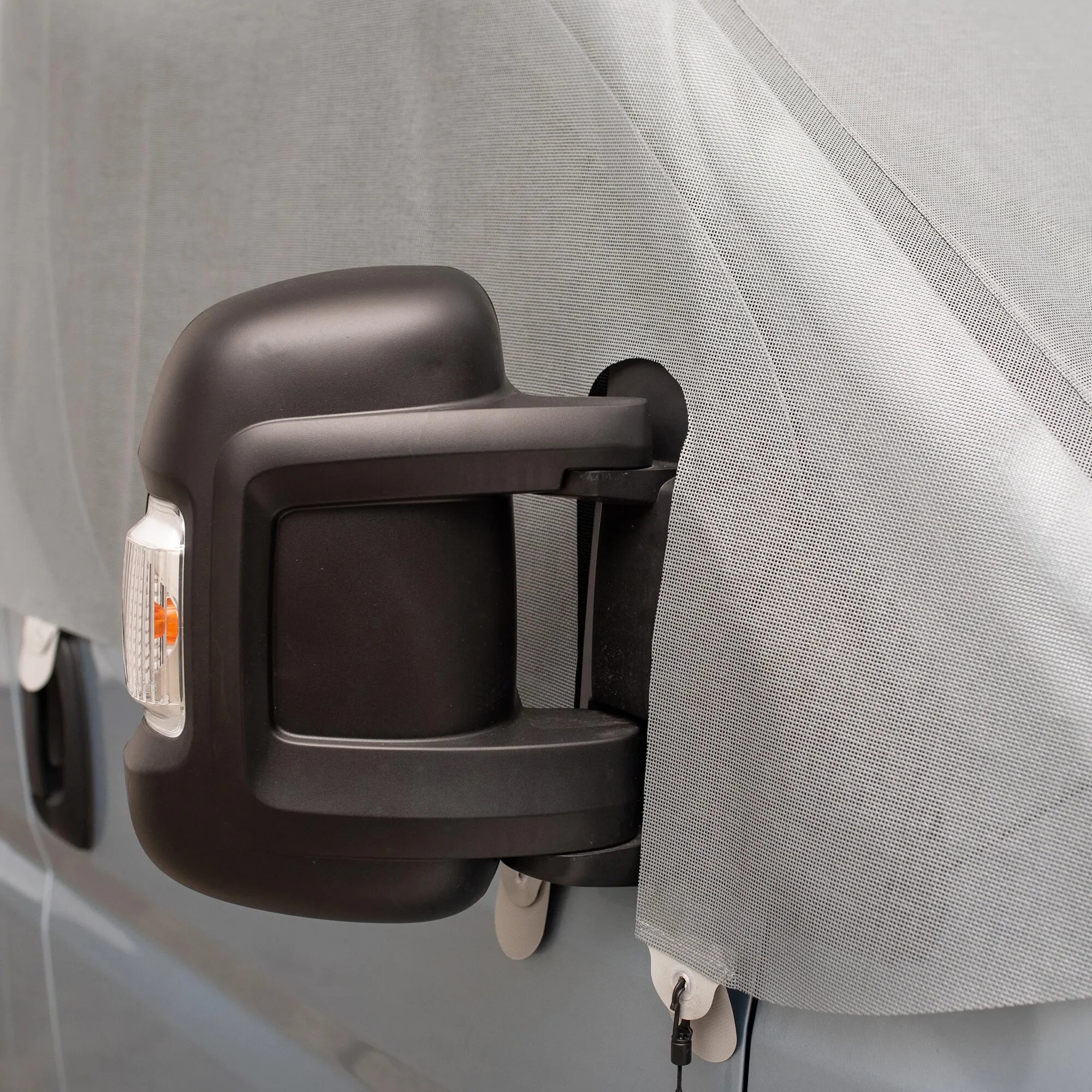 Graue Sonnenschutzmatte als feinmaschiger Screen am Seitenfenster eines VW Crafter Gen. 2 oder MAN TGE neben dem Außenspiegel