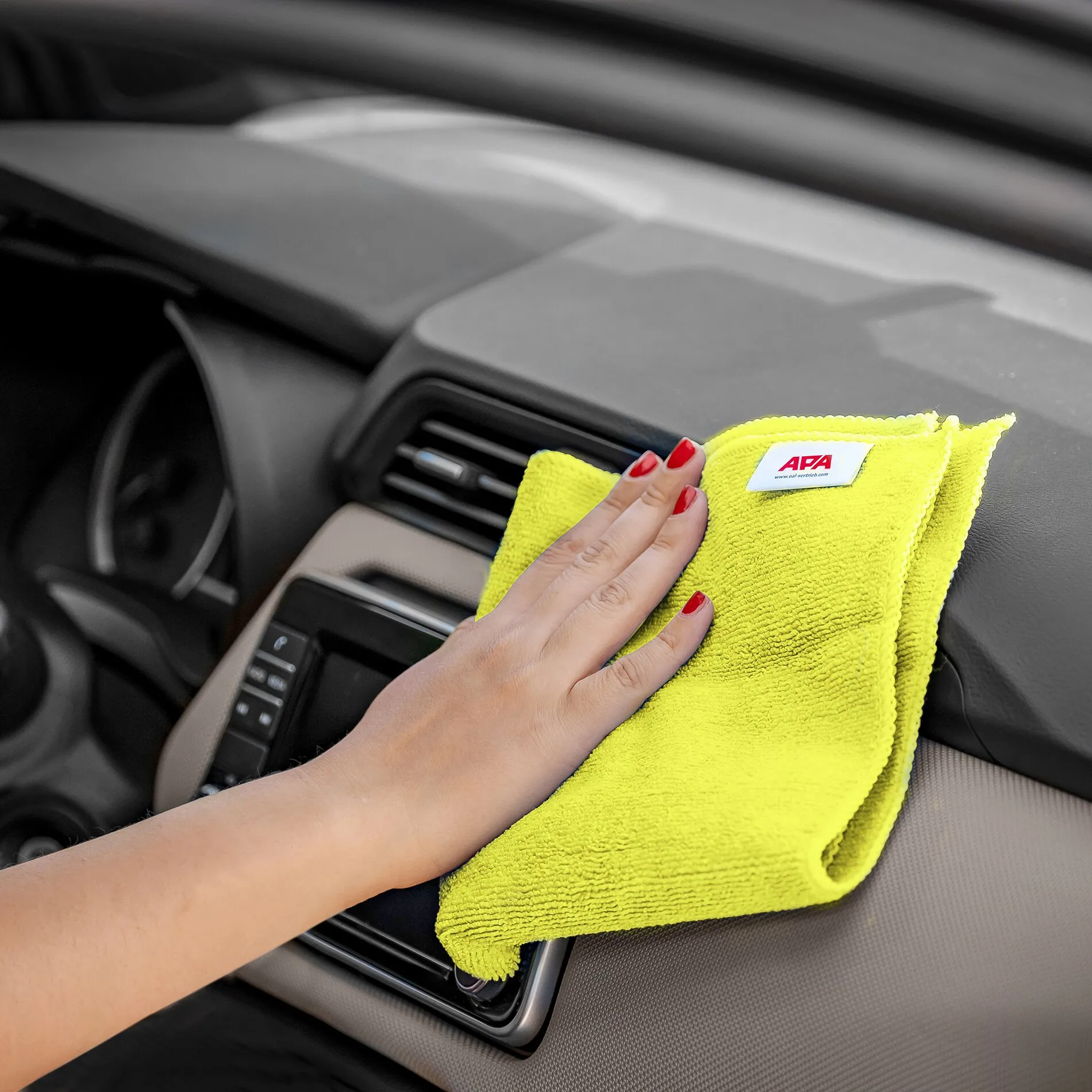 Hand wischt mit gelben APA-Mikrofaser-Reinigungstüchern über das Armaturenbrett eines Autos