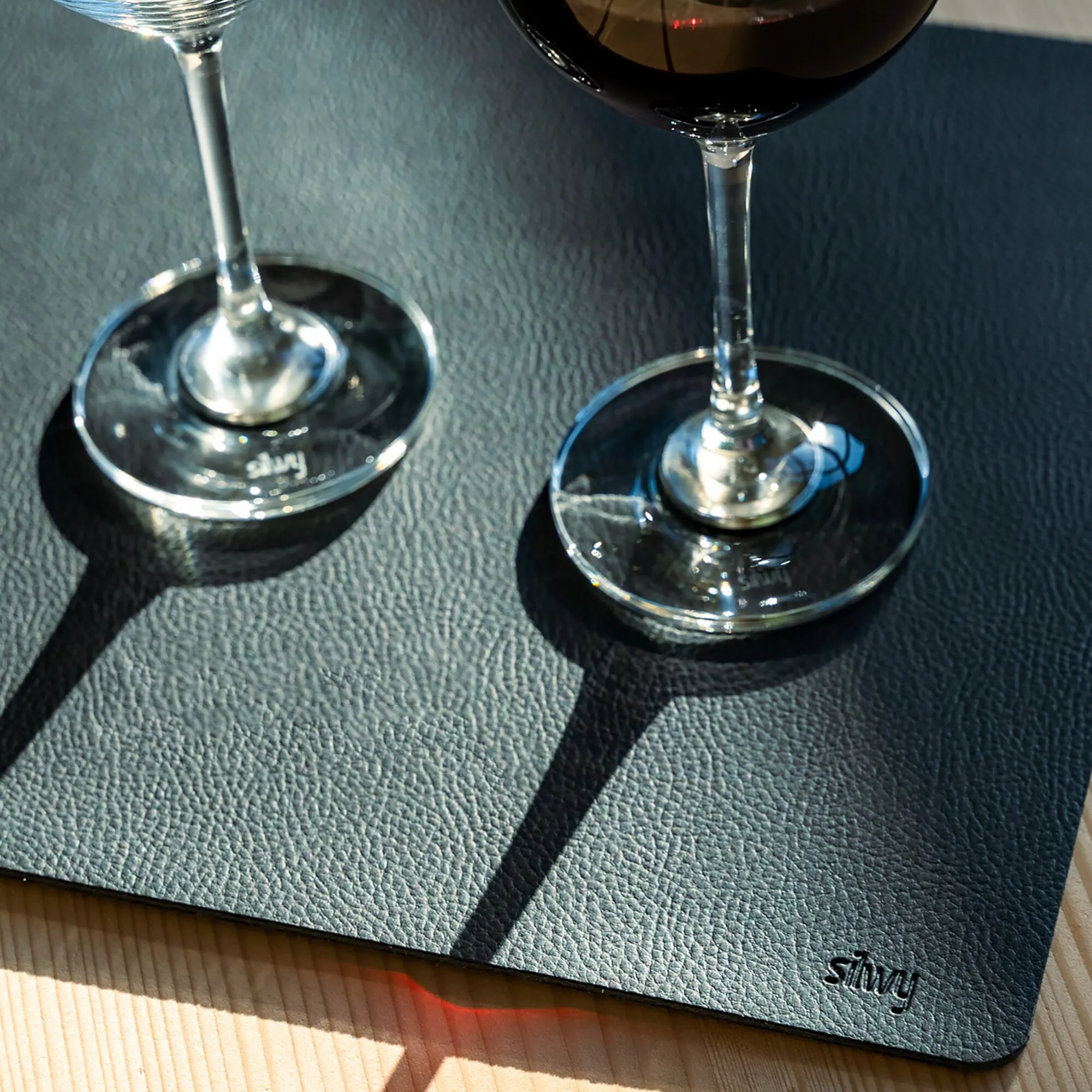 Schwarze Metall-Nano-Gel-Matte mit zwei Weingläsern, rutschfest auf einem Holztisch platziert