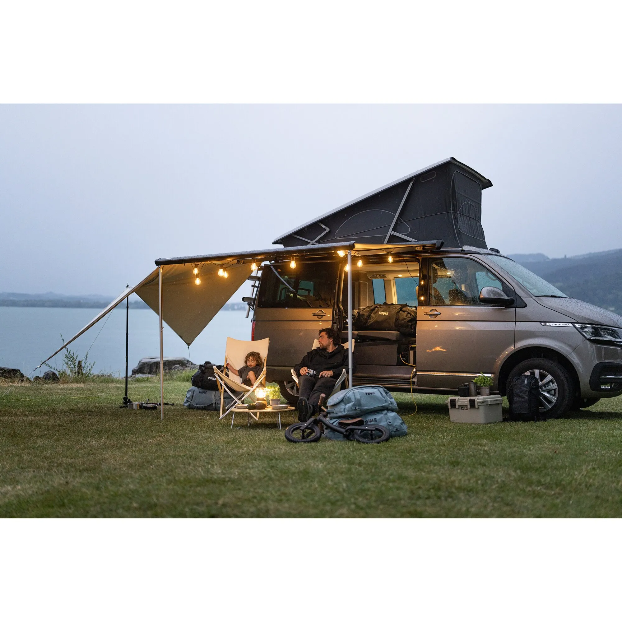 Thule Subsola Medium Panel, 2,50 m, als graue Markise an einem Campervan mit zwei Personen am See aufgestellt