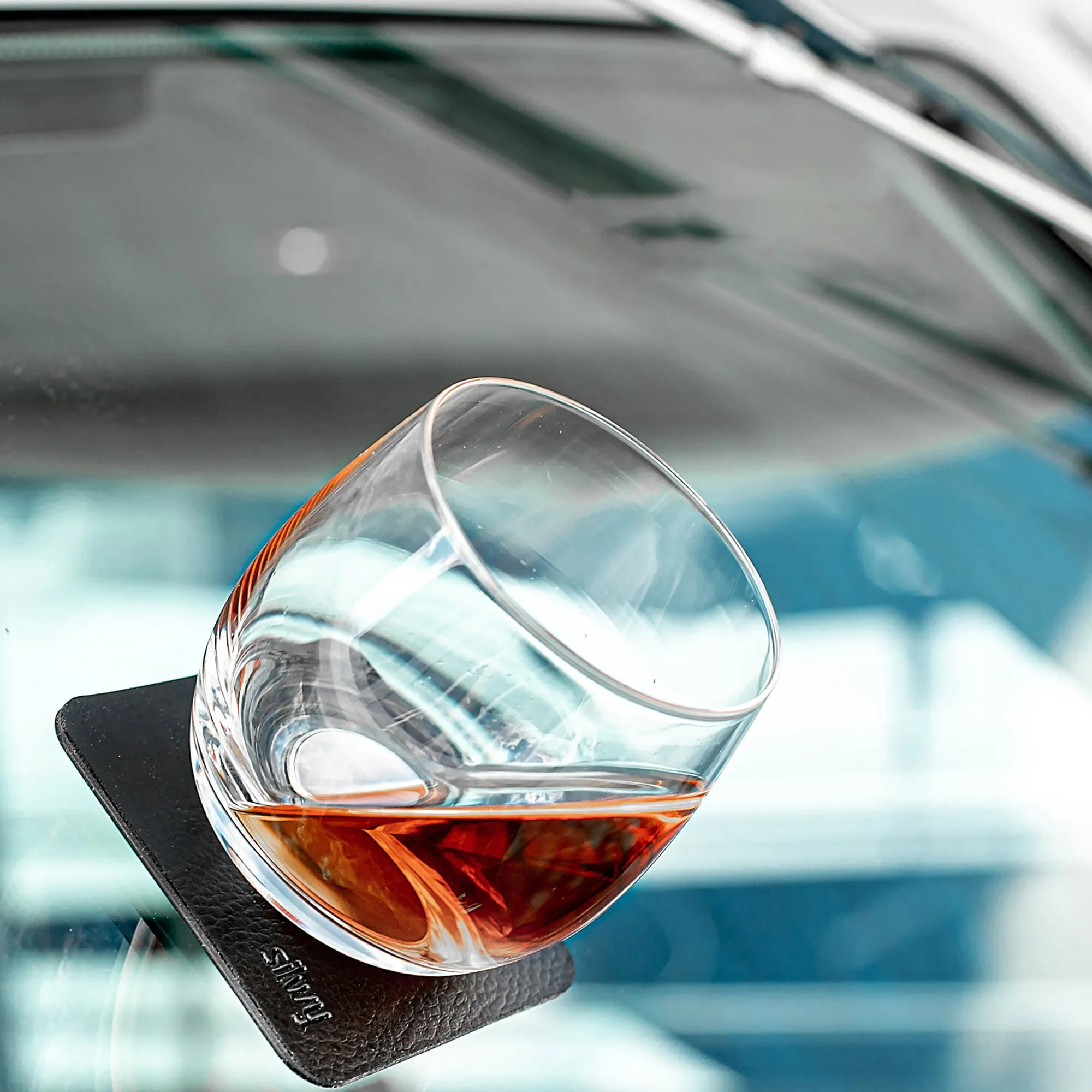 Facettiertes, klares Whisky-Kristallglas mit bernsteinfarbenem Whisky und Eiswürfel auf schwarzem Untersetzer