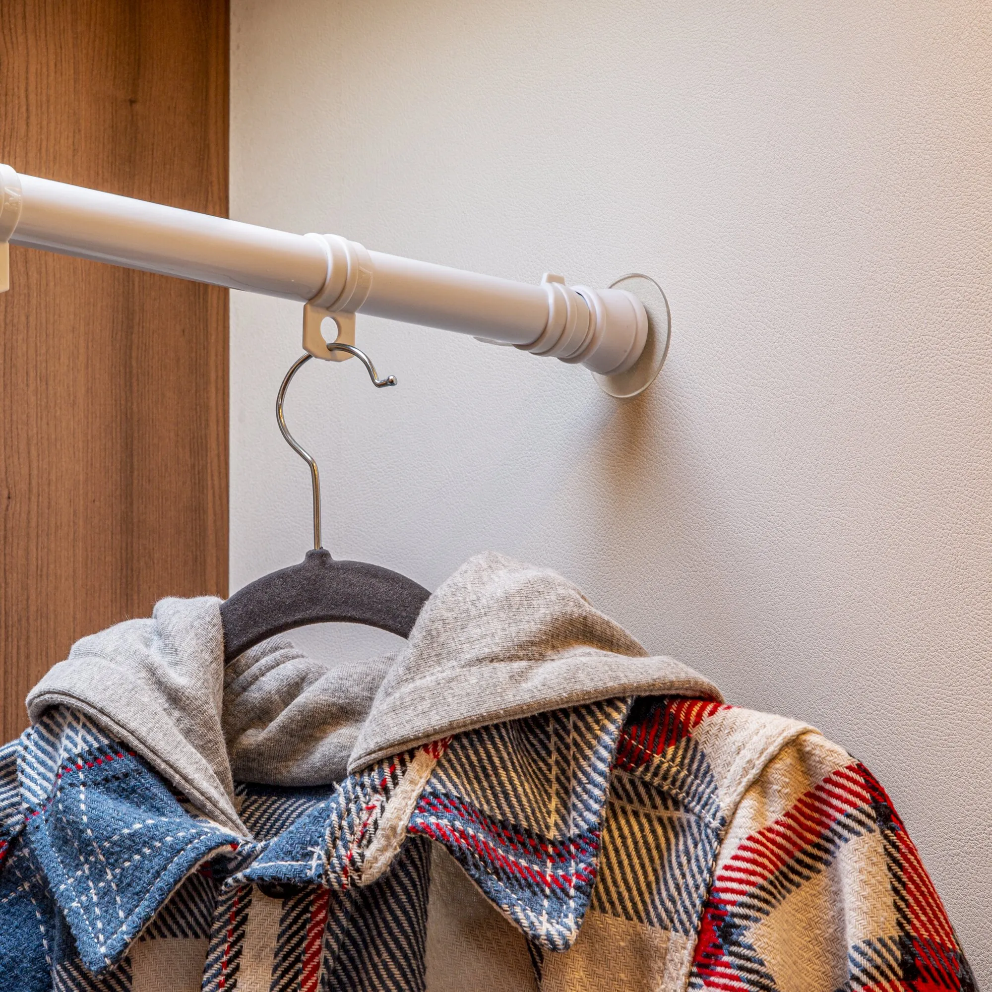 Weiße Teleskop-Kleiderstange mit Wandhalterung und Kleiderbügeln, an denen mehrere karierte Kleidungsstücke hängen