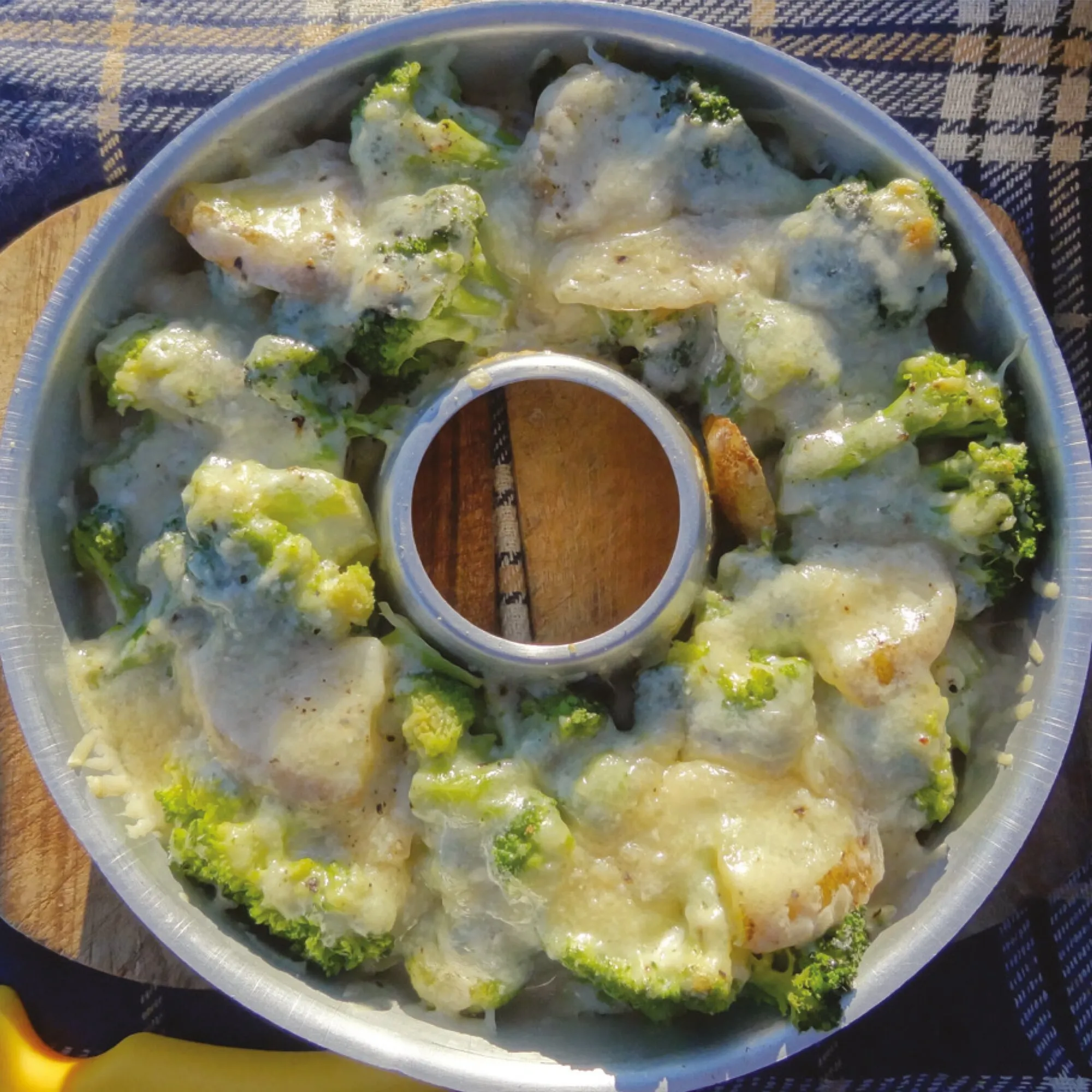 Brokkoli-Kartoffel-Auflauf mit geschmolzenem Käse im runden Omnia-Backofen mit Mittelöffnung, auf einem Holztisch angerichtet