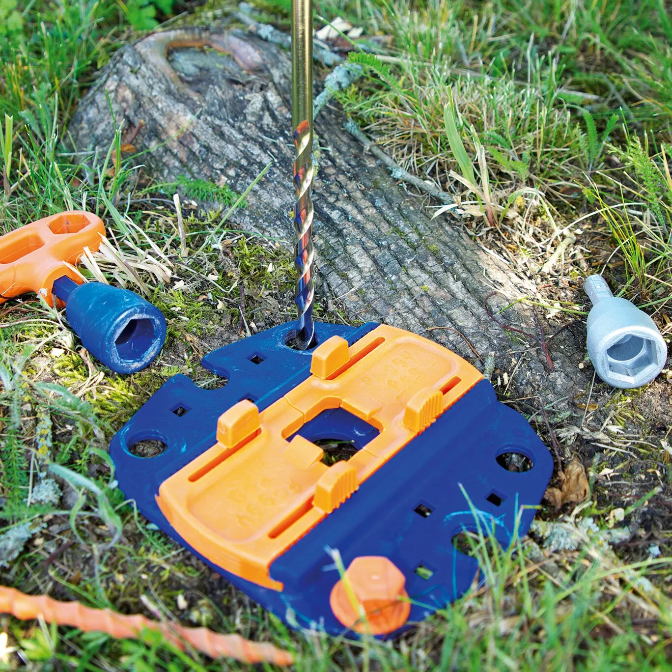 Blau-orange Bohrschablone des Vorbohrsets Pre Drill mit eingesetztem Spiralbohrer auf einem Baumstumpf im Freien