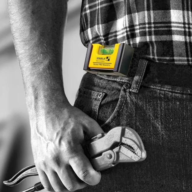 Gelbe magnetische Pocket-Wasserwaage von Stabila am Gürtel einer Handwerkerin mit Rohrzange in der Hand