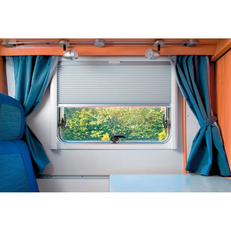 Graues Rollo REMIflair IV, 166,40 × 80 cm, halb geschlossen an einem Wohnmobilfenster mit blauen Vorhängen und Waldblick