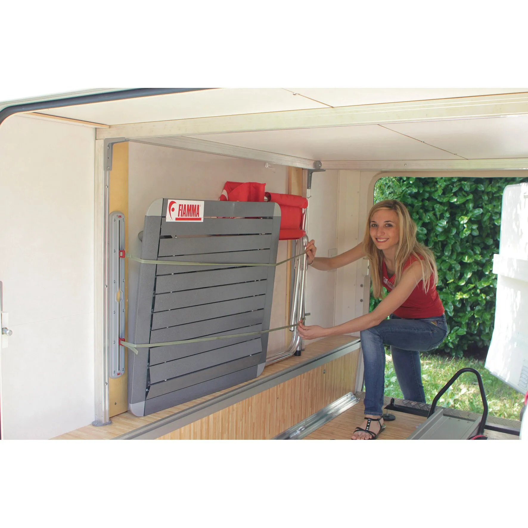 Fiamma Cargo Strap befestigt mit zwei grünen Gurten ein graues, zusammengeklapptes Campingmöbel in der Wohnmobil-Heckgarage