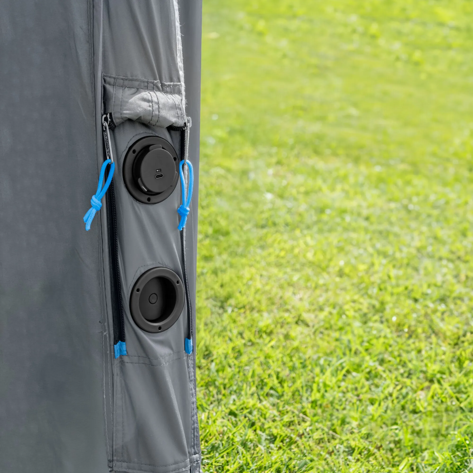 Detailaufnahme des grauen Heckklappenzelts Indipendence mit zwei runden schwarzen Verschlüssen und blauen Zugseilen vor einer grünen Wiese