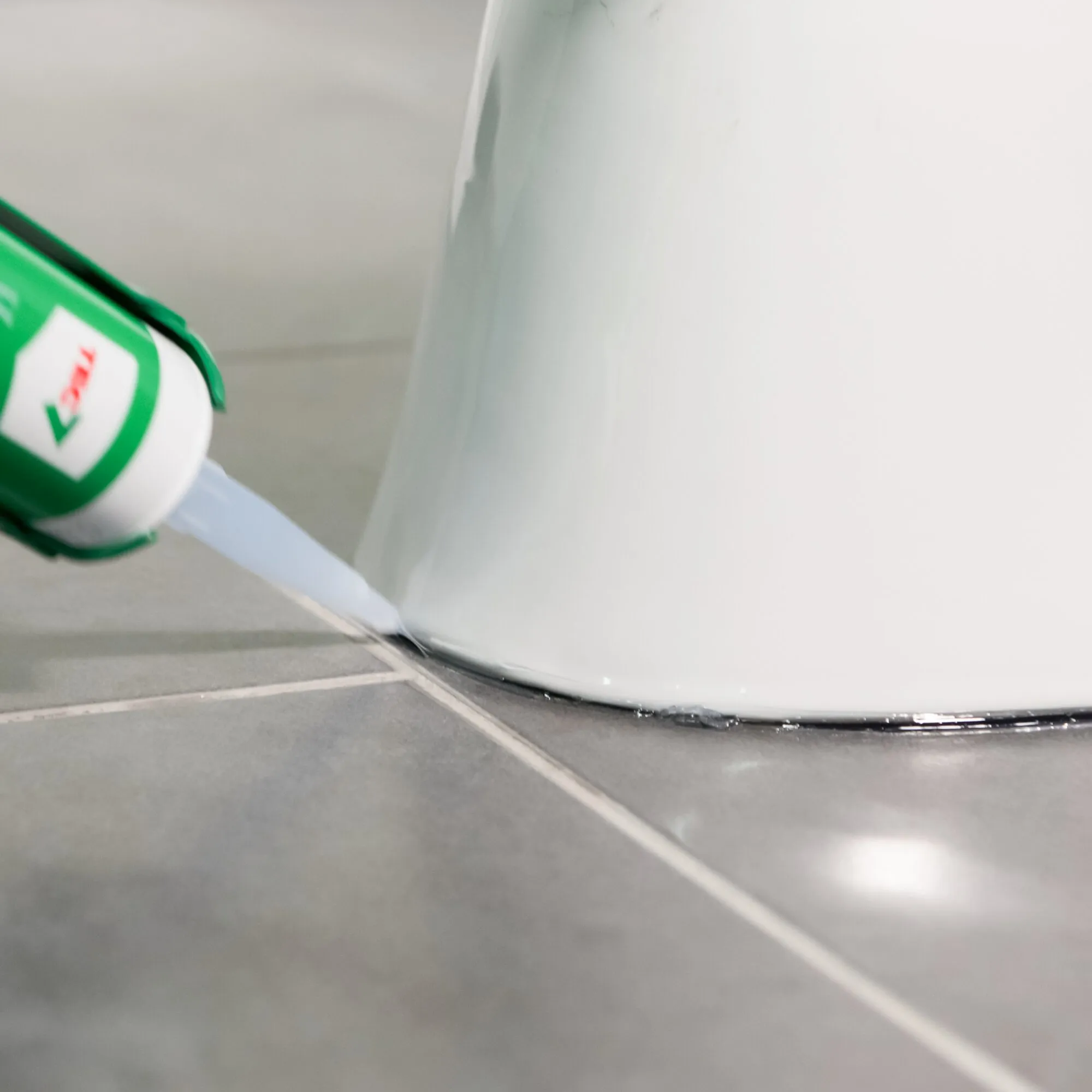 Kleb- und Dichtstoff TRANSCLEAR wird mit einer Kartusche als Dichtnaht am Fuß eines weißen Sanitärbeckens aufgetragen