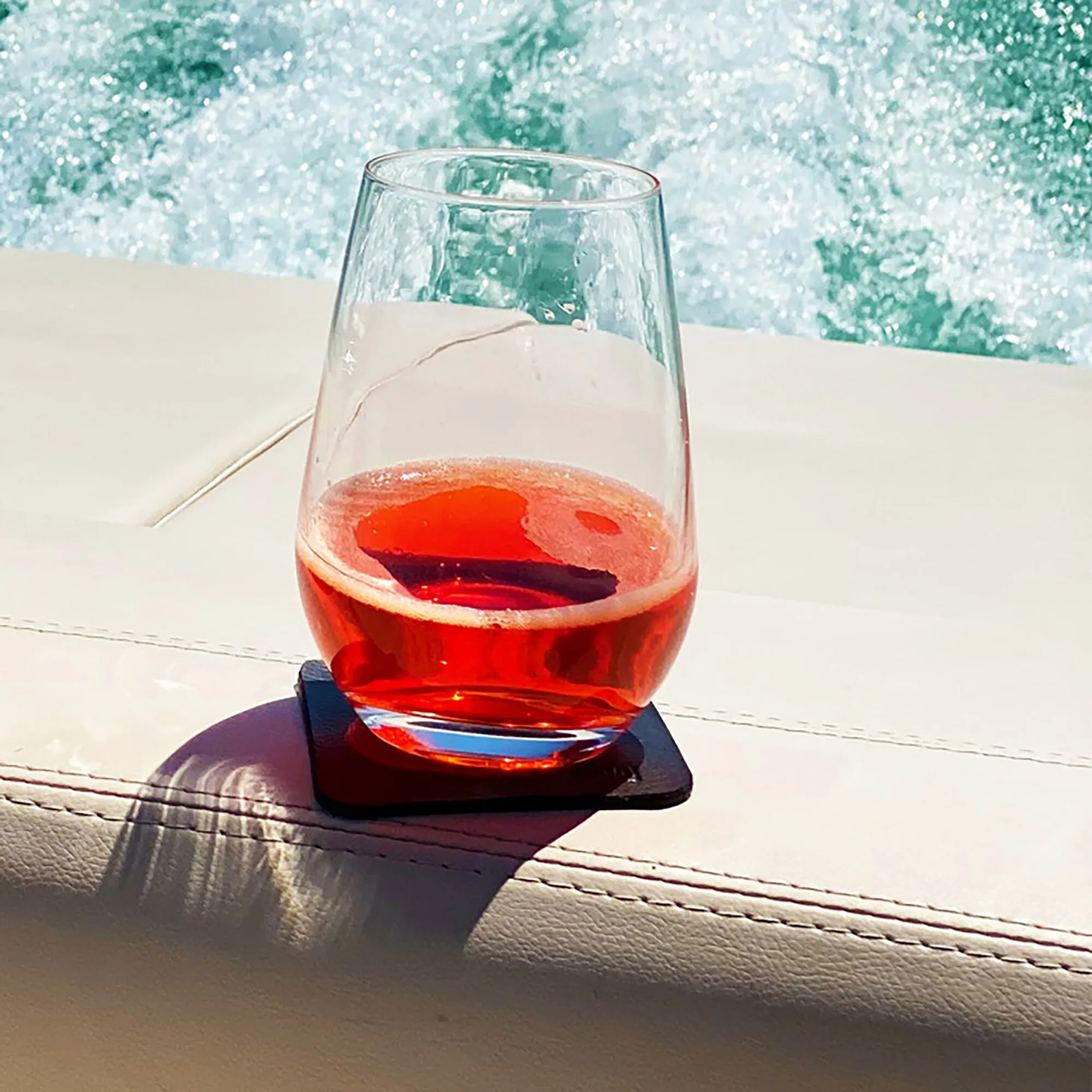 Transparentes Magnet-Kristallglas für Longdrinks mit rotem Getränk auf schwarzem Untersetzer am hellen Tisch am Fensterેણ