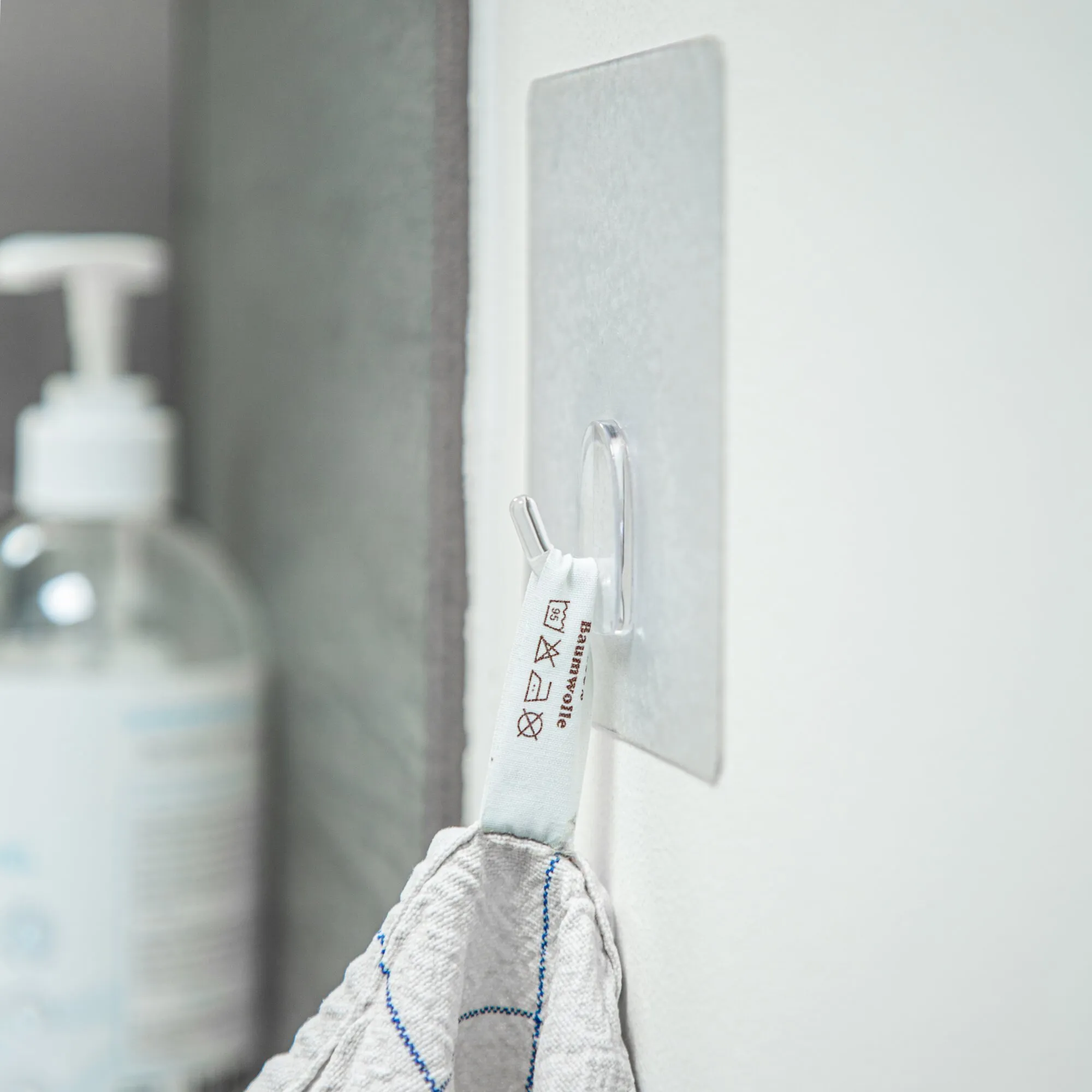 Transparenter XL-Haken mit rechteckiger Klebefläche an einer hellen Wand, hält ein weißes Reinigungstuch bereit