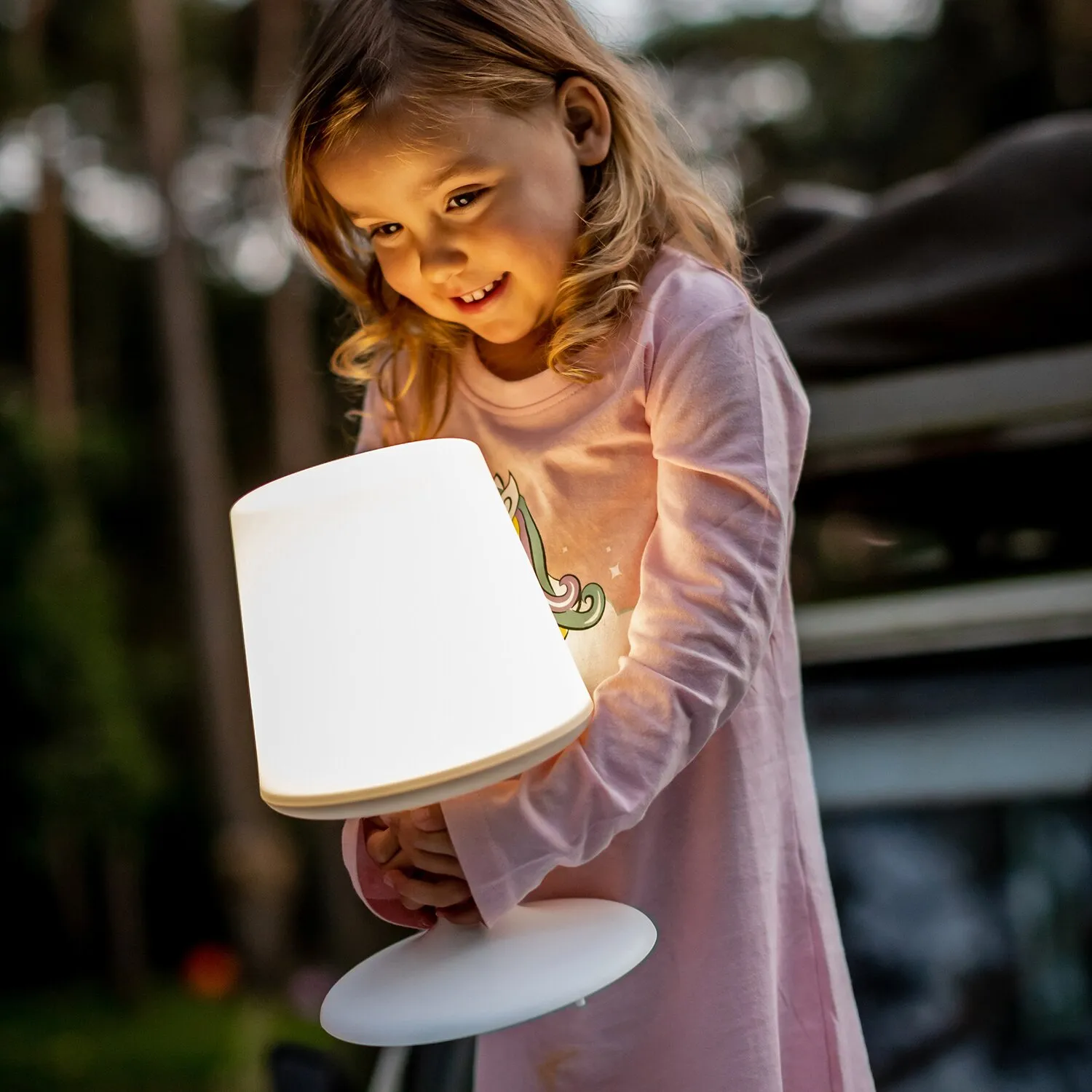 Ein Mädchen hält die leuchtende weiße Tischleuchte Light to Go mit zylindrischem Schirm und rundem Fuß in den Händen