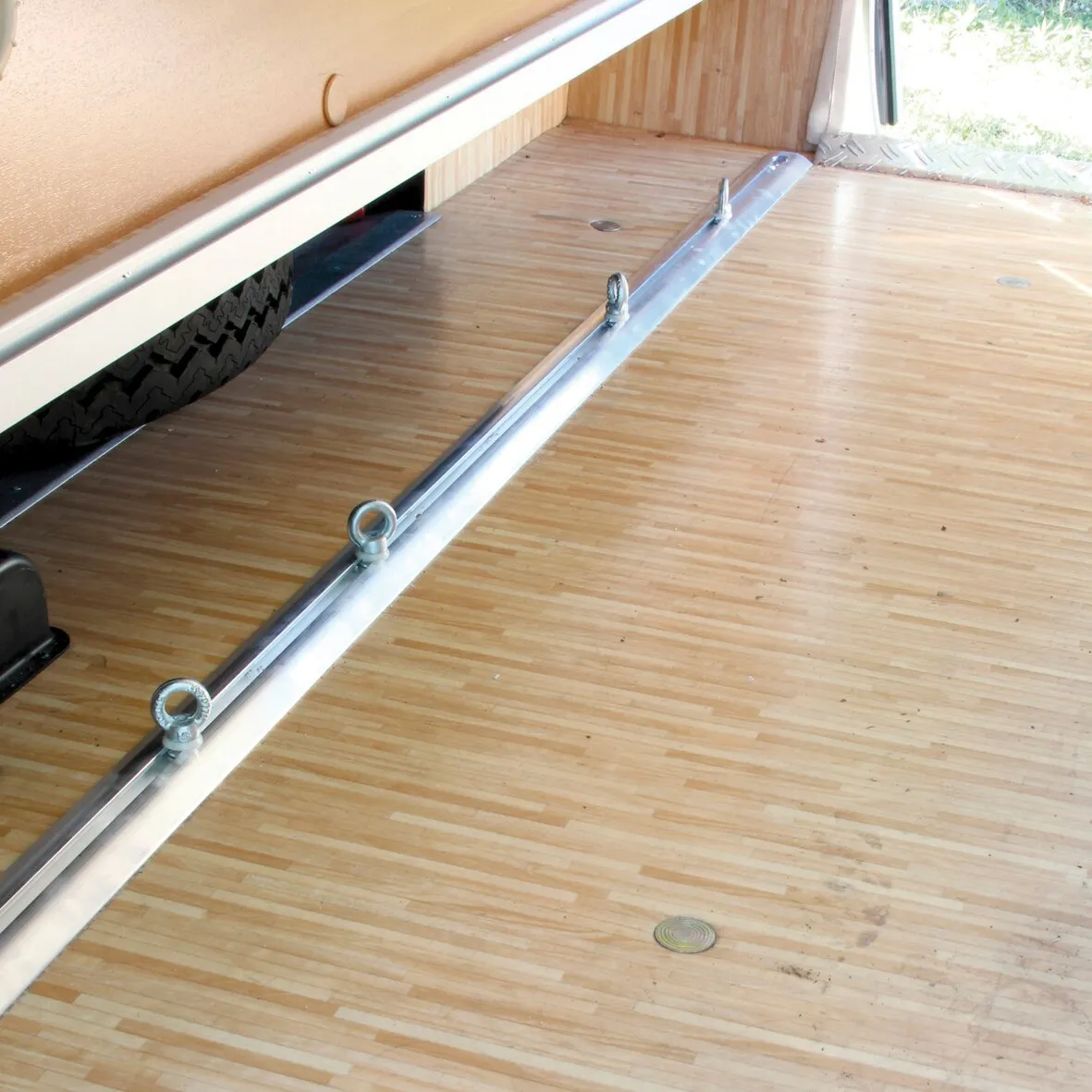 Verzurrschiene aus Metall mit mehreren Befestigungsösen auf dem Holzboden eines Fahrzeuganhängers, Detailansicht der Multifunktionsleiste Garage-Bars 200 cm