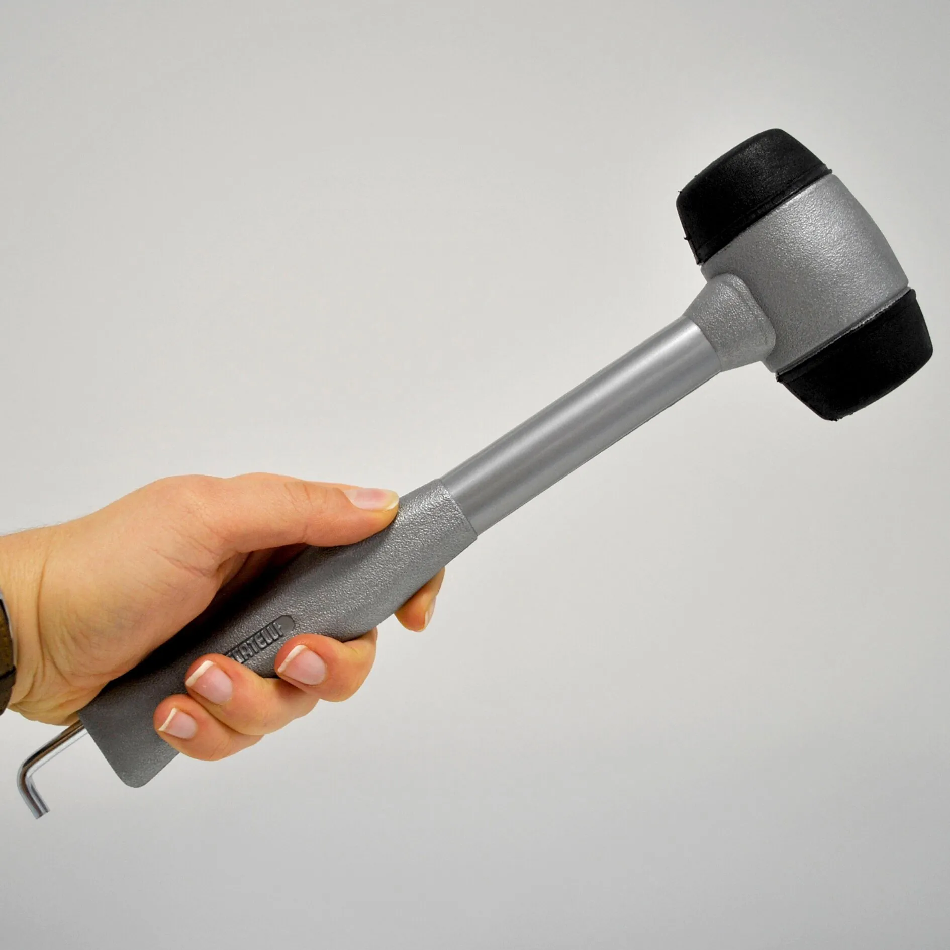 Grauer Kunststoffhammer mit schwarzen Schlagflächen, von einer Hand am ergonomischen Griff gehalten