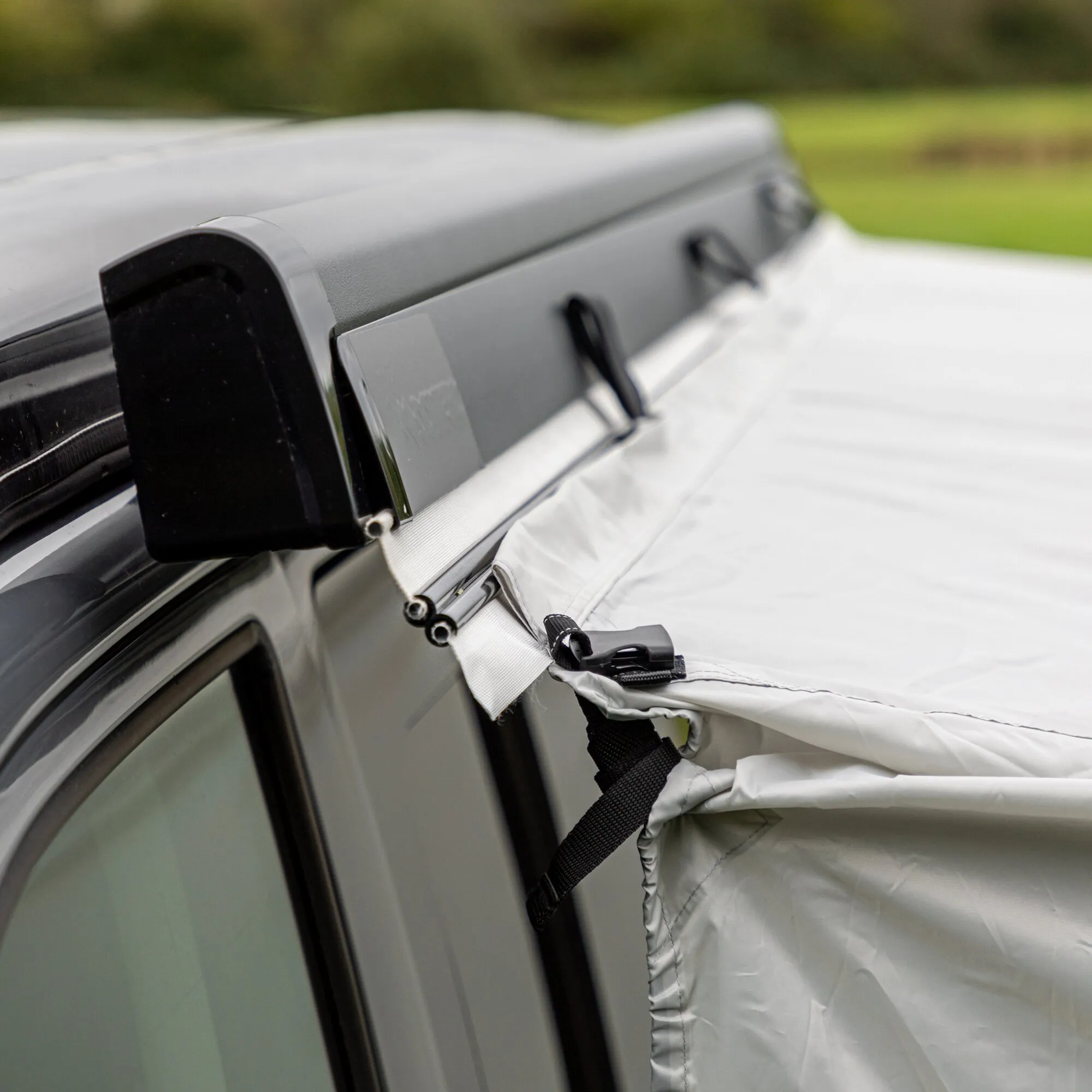 Detailaufnahme des grauen Anschlussprofils am Fahrzeug mit befestigtem weißen Stoff des Busvorzelts Journeymaster Deluxe L