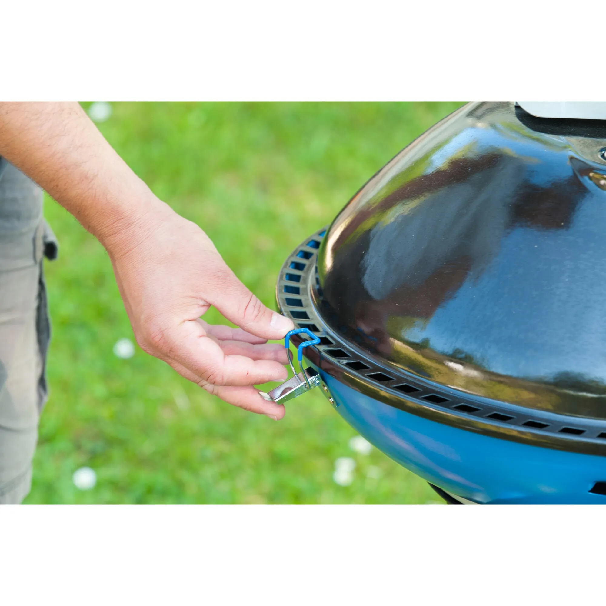 Detailaufnahme des blauen Party Grill 600 R mit geschlossenem Deckel, während eine Person die seitliche Befestigung bedient