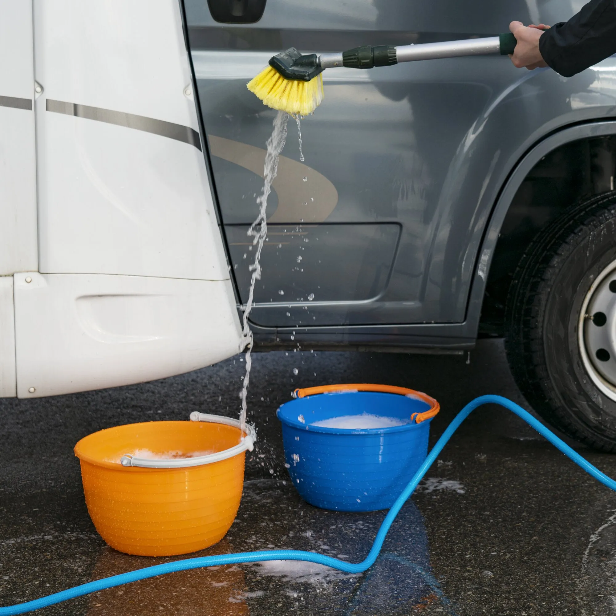 Oranger Vielzweckeimer Vinis wird beim Reinigen eines Fahrzeugs mit Wasser befüllt, daneben steht ein blauer Eimer