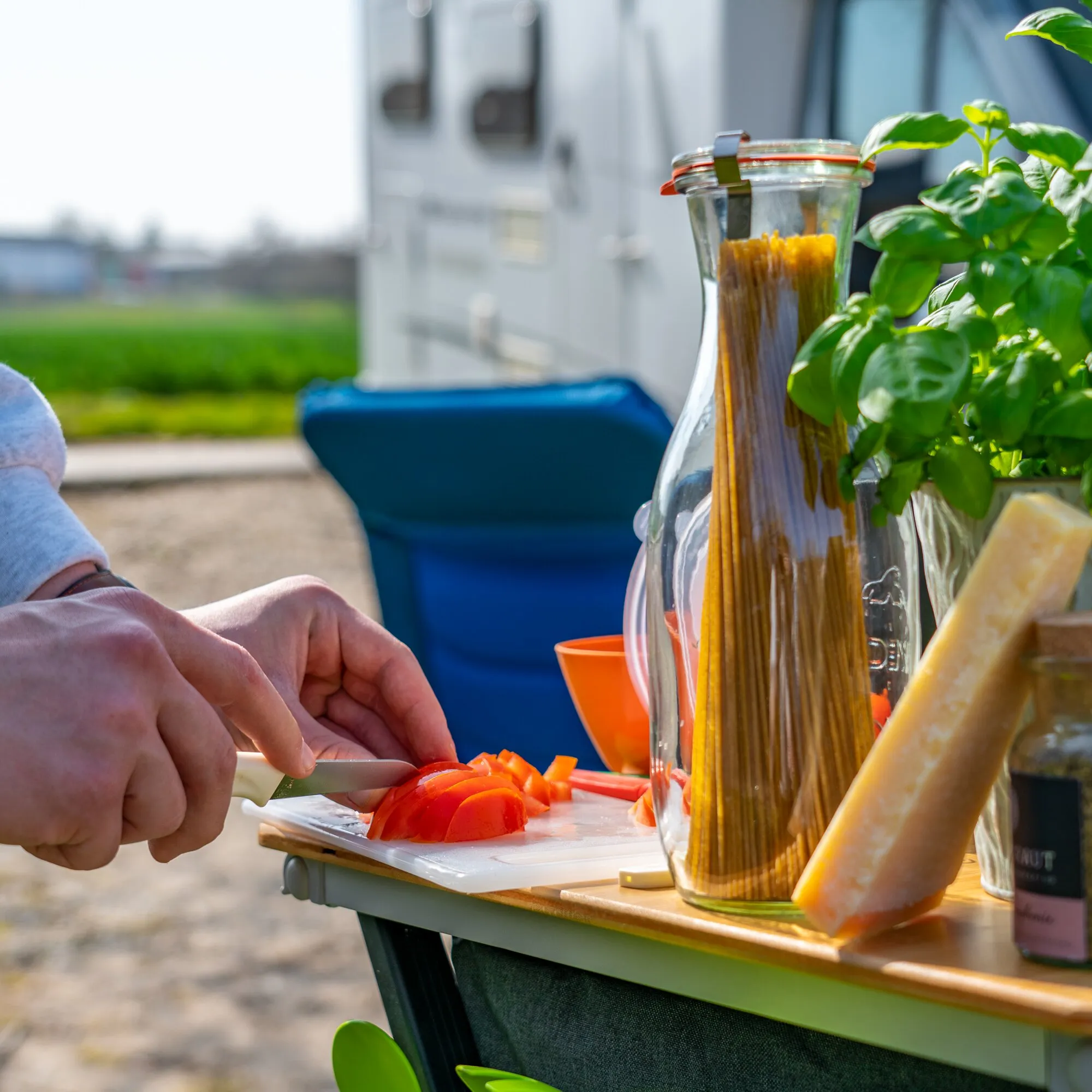 Hände schneiden Tomaten auf einem weißen Schneidebrett; darunter liegt ein holzfarbenes Brett des Schneidebrett-Sets