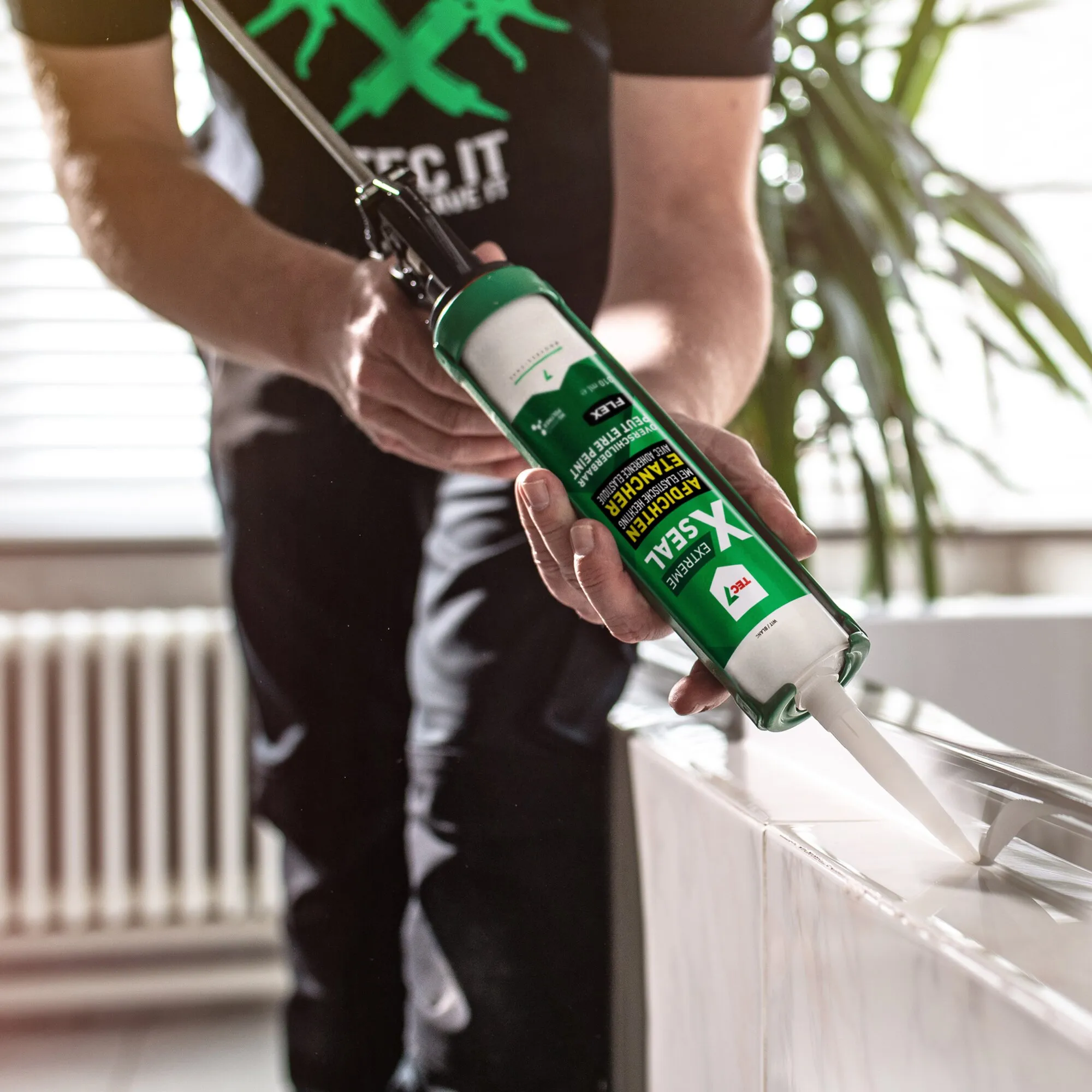Person trägt weißen Dichtstoff XSEAL EXTREME mit grüner Kartusche auf eine Fensterfuge auf