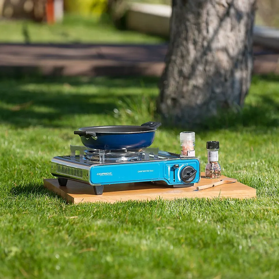 Blauer Campingaz Camp'Bistro DLX Campingkocher mit Pfanne auf einem Holzbrett im Garten, daneben Gewürzstreuer