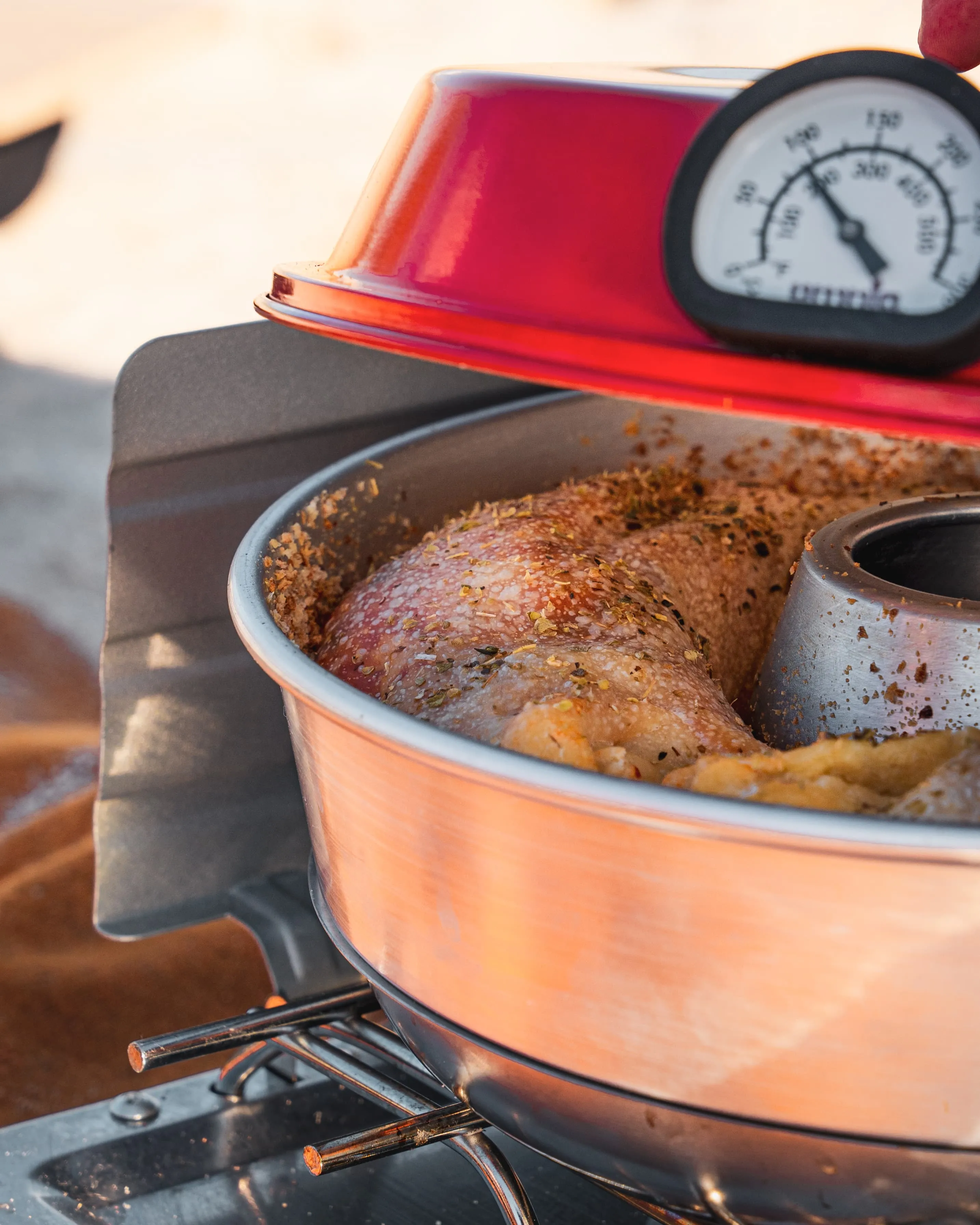 Rotes Grillthermometer mit analoger Anzeige steckt in gewürztem Fleisch auf einem Gasgrill