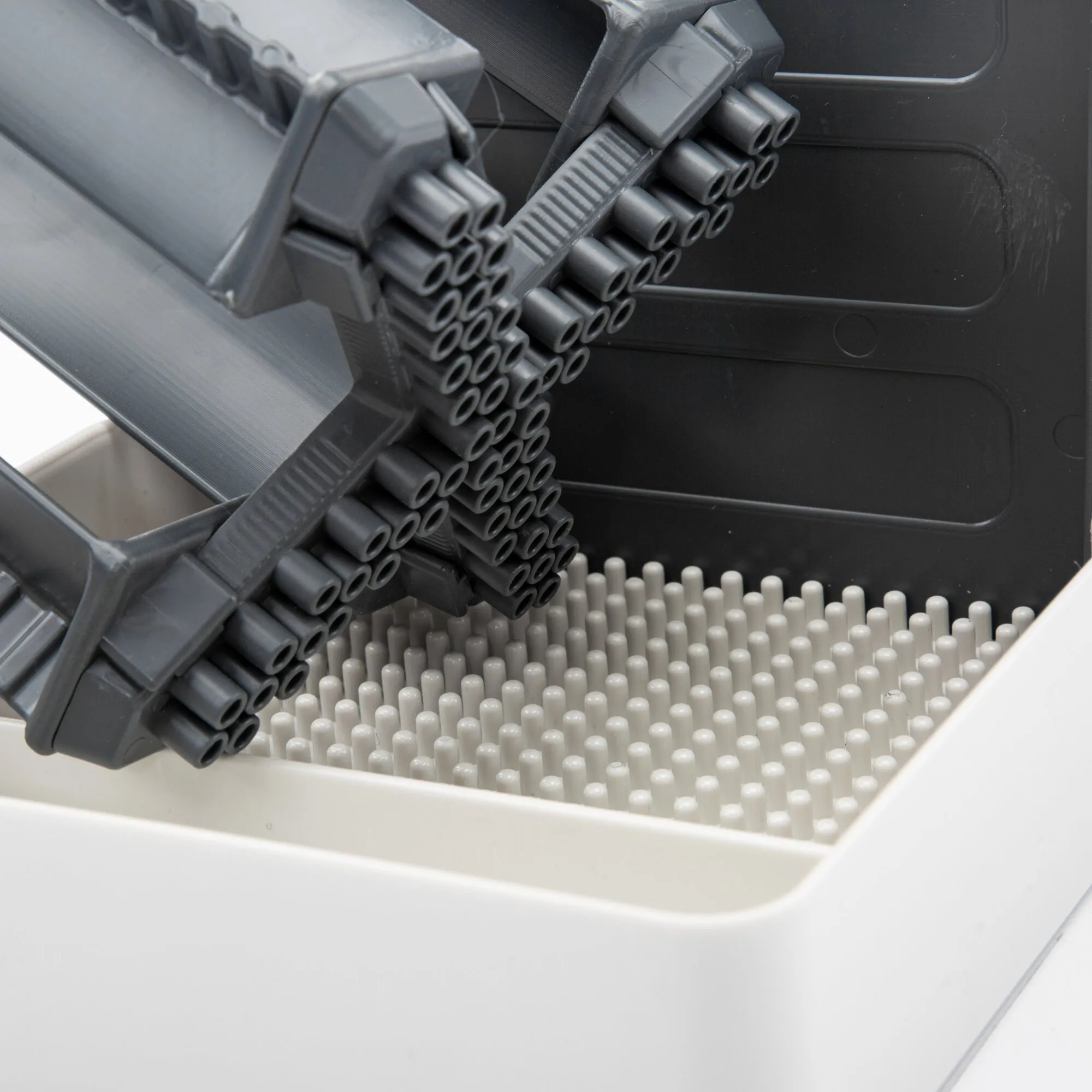 Detailansicht des hellgrauen Flaschenhalters Multi Tray OELE im Geschirrspüler über einem weißen Stiftraster