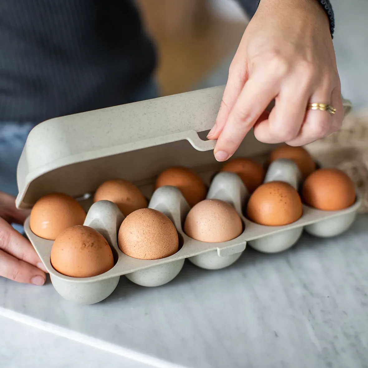 Geöffnete sandfarbene Eierbox EGGS TO GO mit braunen und weißen Eiern, auf einer Küchenarbeitsfläche von Händen gehalten