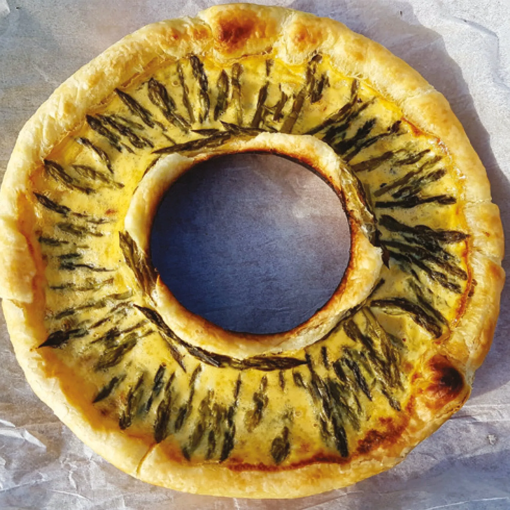 Goldbraun gebackene Quiche im Ring mit grünem Spargel auf Backpapier, aus dem Kochbuch für den Omnia Backofen