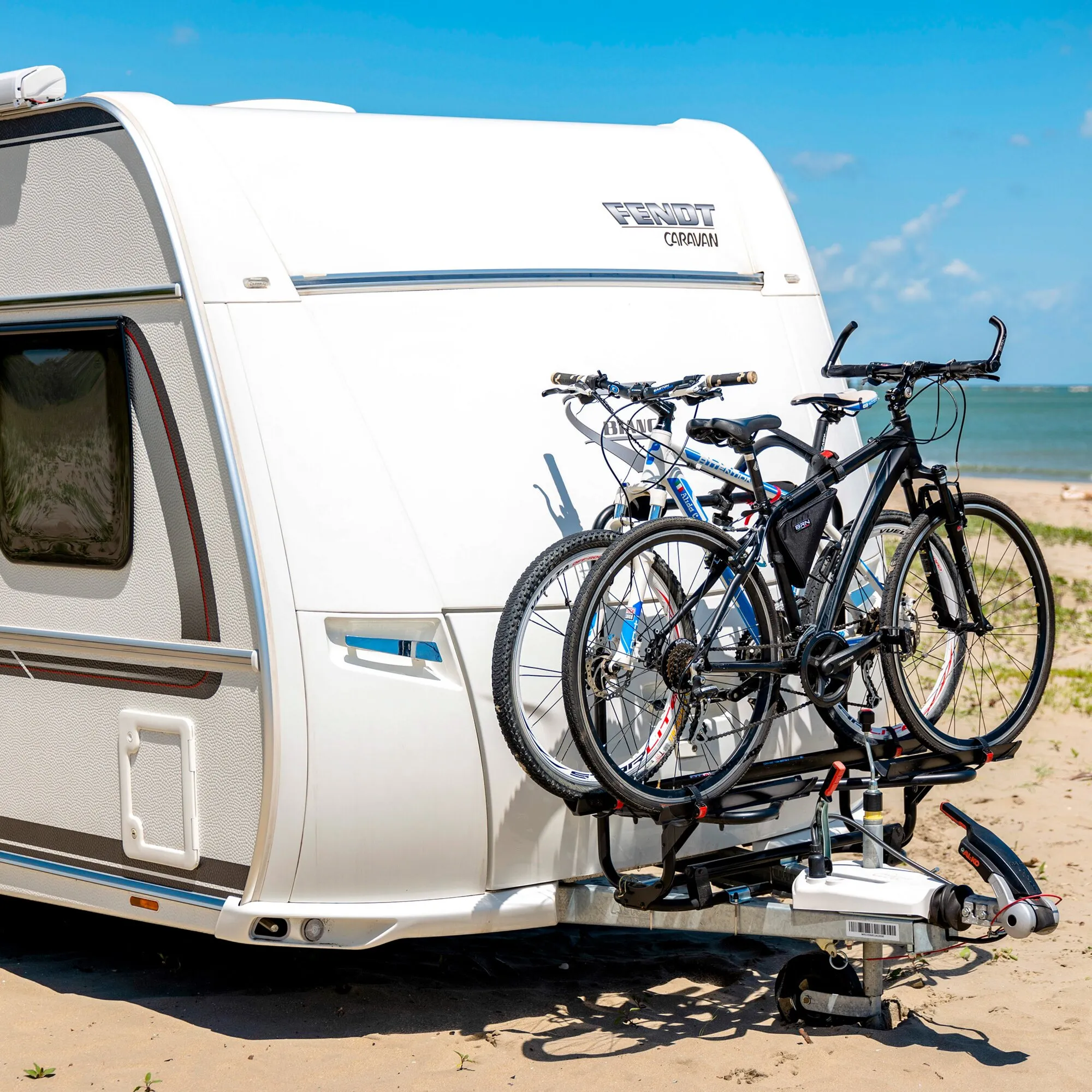 Schwarzer Deichselträger Carry-Bike Caravan XL A Pro 200 mit zwei Fahrrädern an einem weißen Wohnwagen am Strand